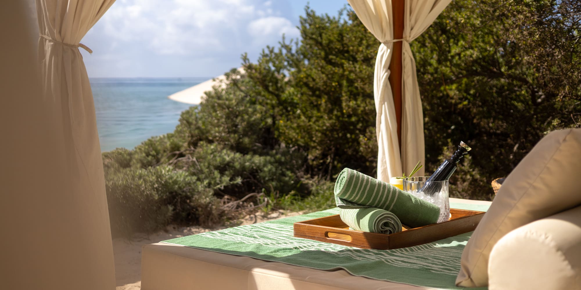 Luxury beach cabana with ocean view, green towels, and chilled champagne.
