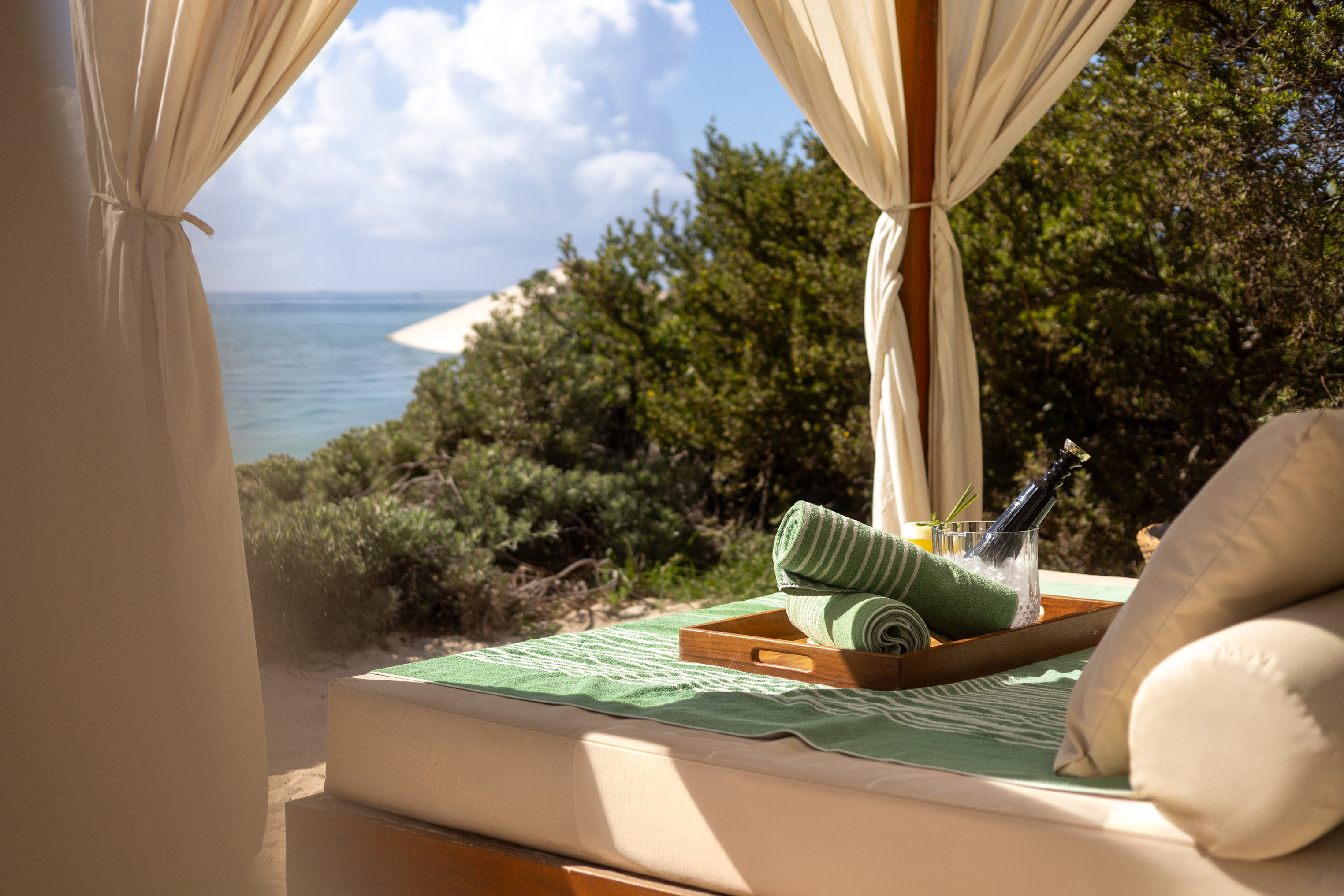 Luxury beach cabana with ocean view, green towels, and chilled champagne.