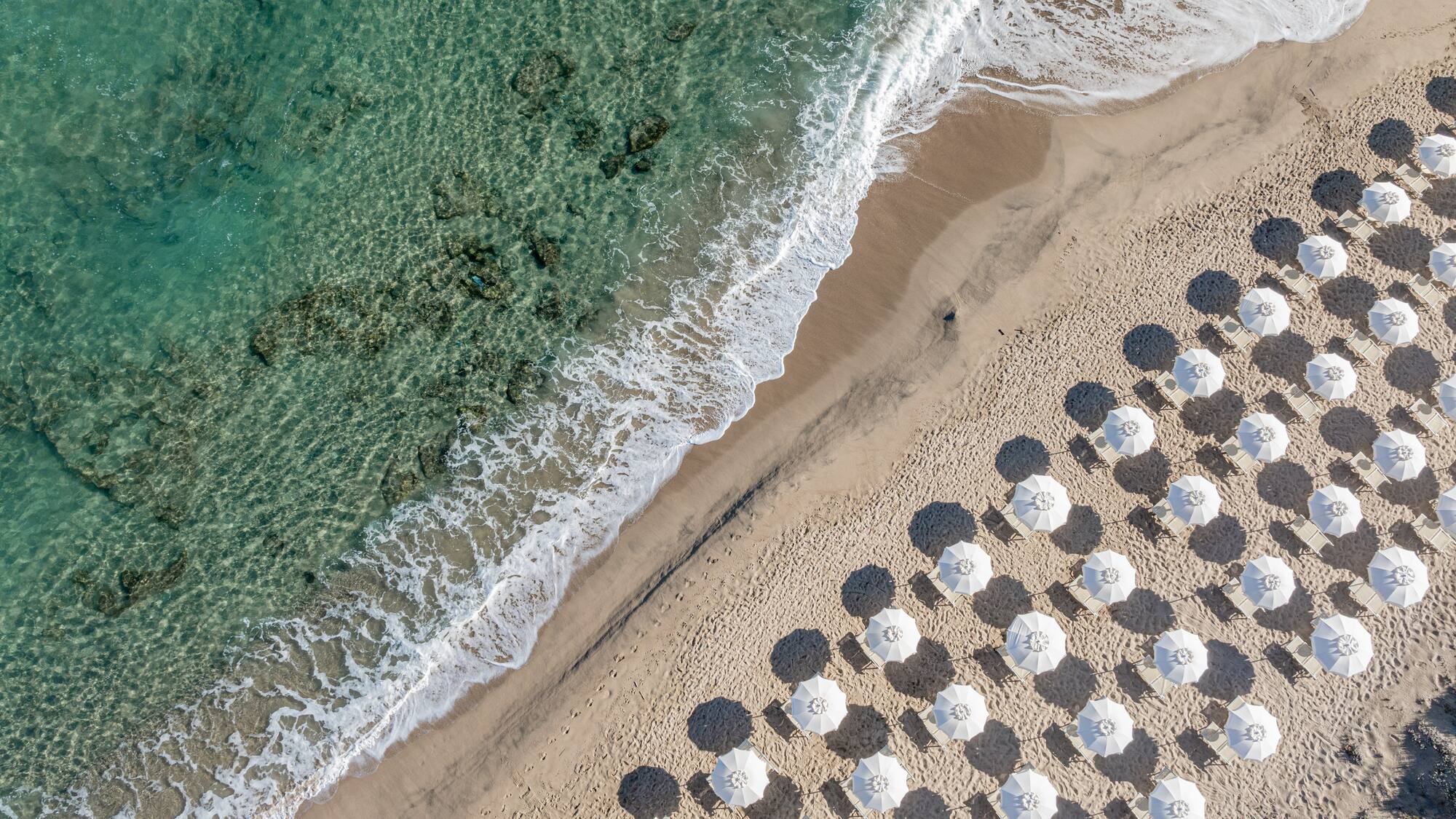 Aerial beach view: turquoise sea, sandy shore, white umbrellas.
