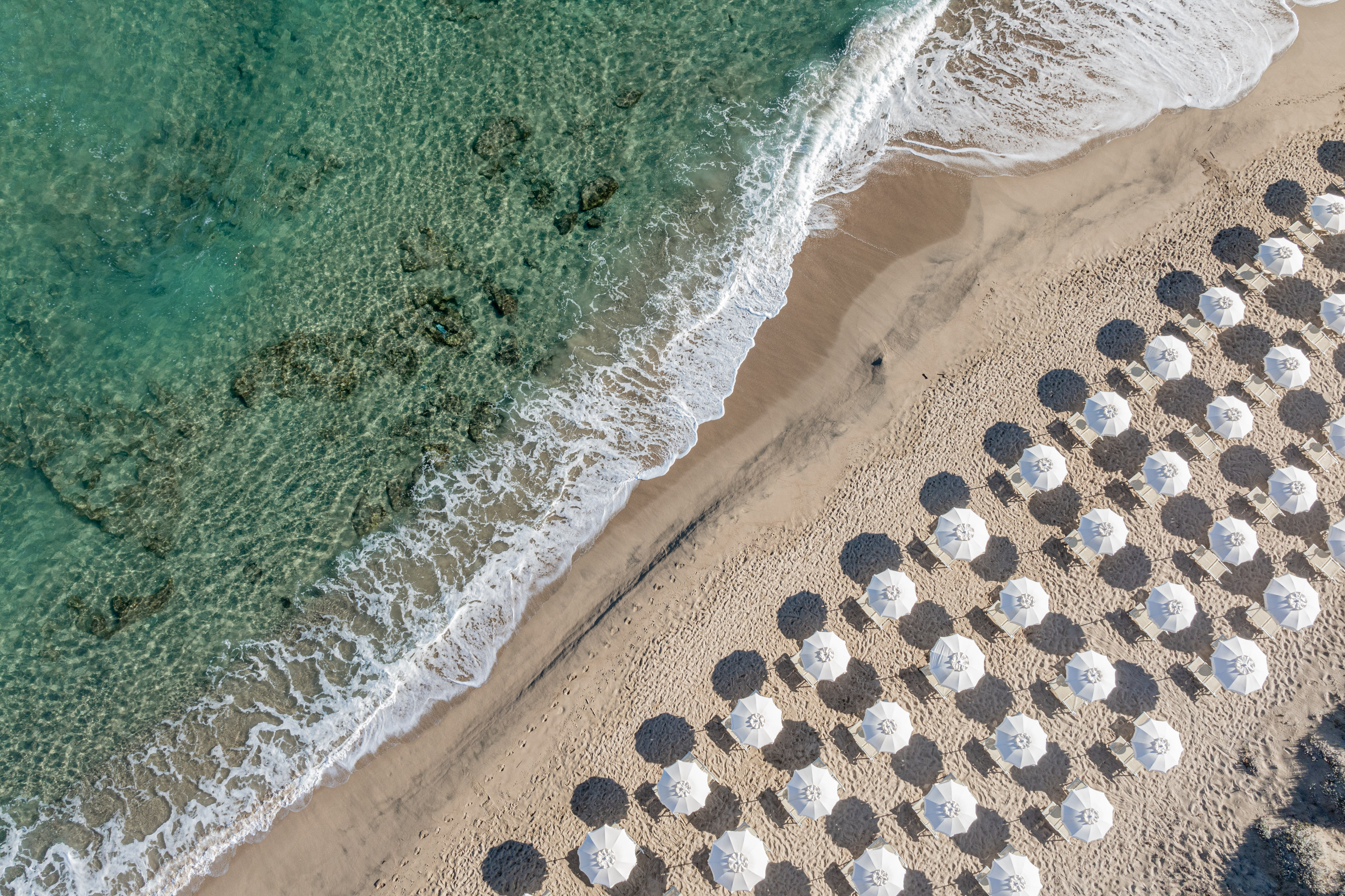 Aerial beach view: turquoise sea, sandy shore, white umbrellas.