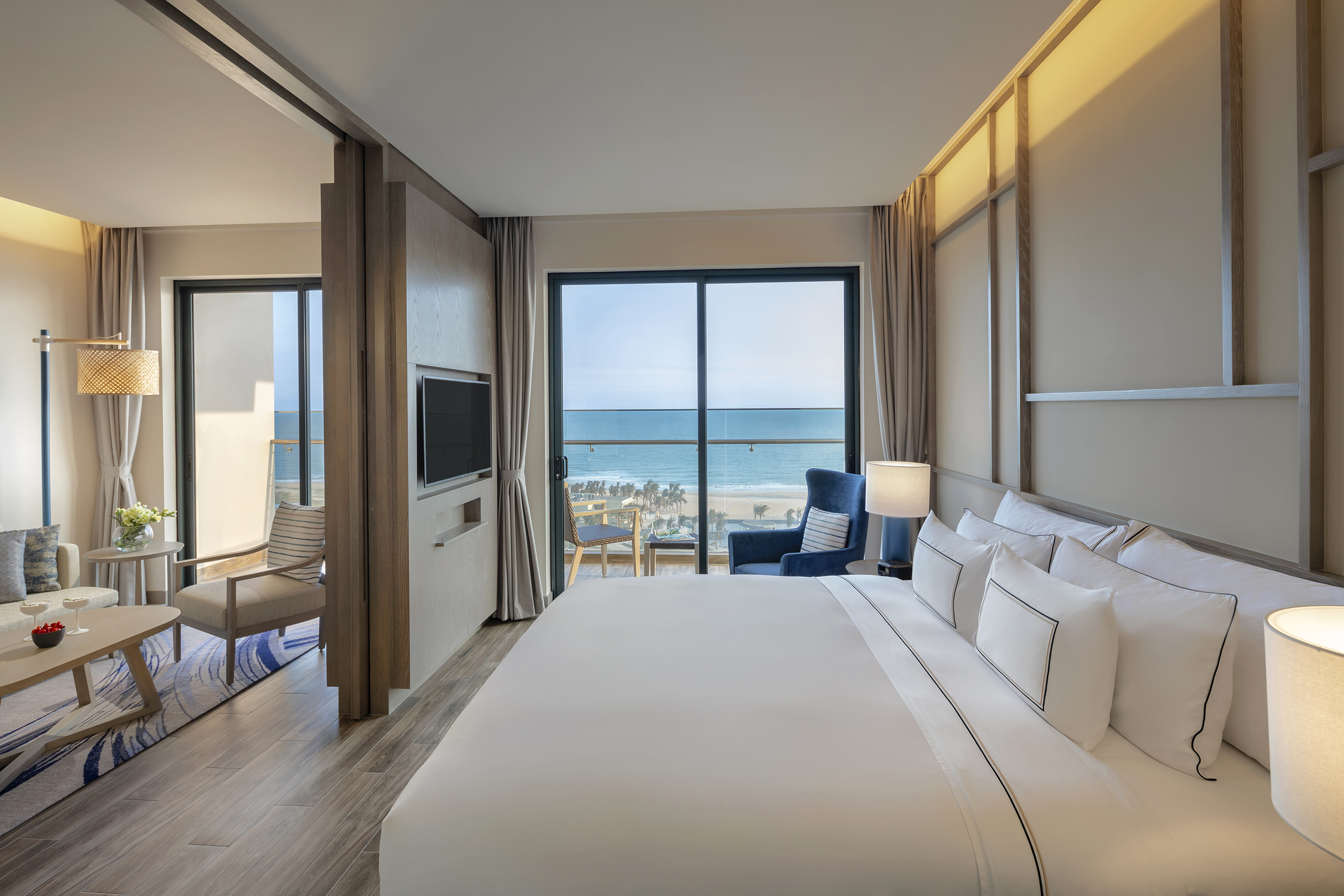 Modern hotel suite with ocean view balcony and separate living area.