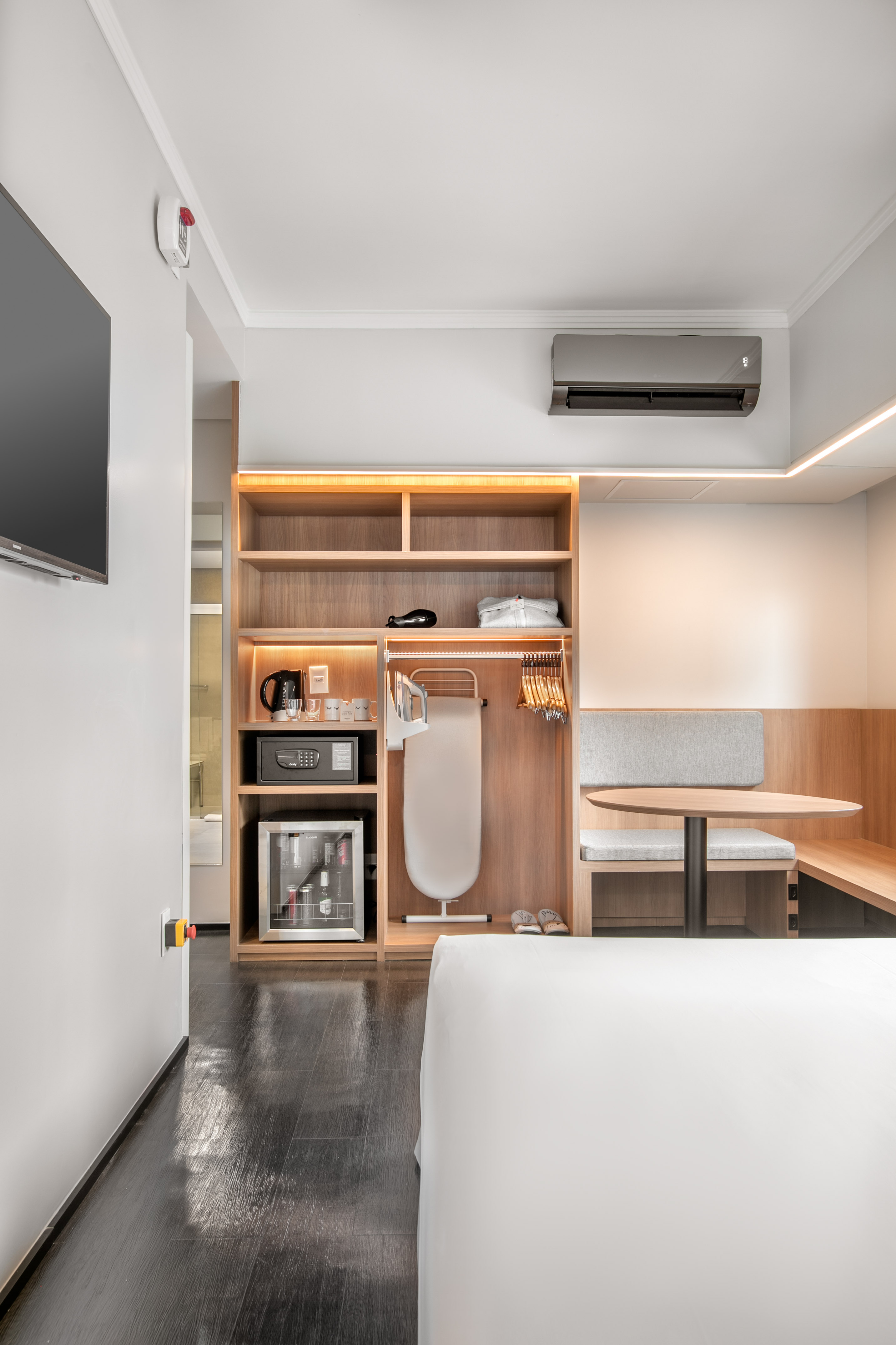 Modern hotel room: bed, integrated wood unit, mini-fridge, and workspace table.