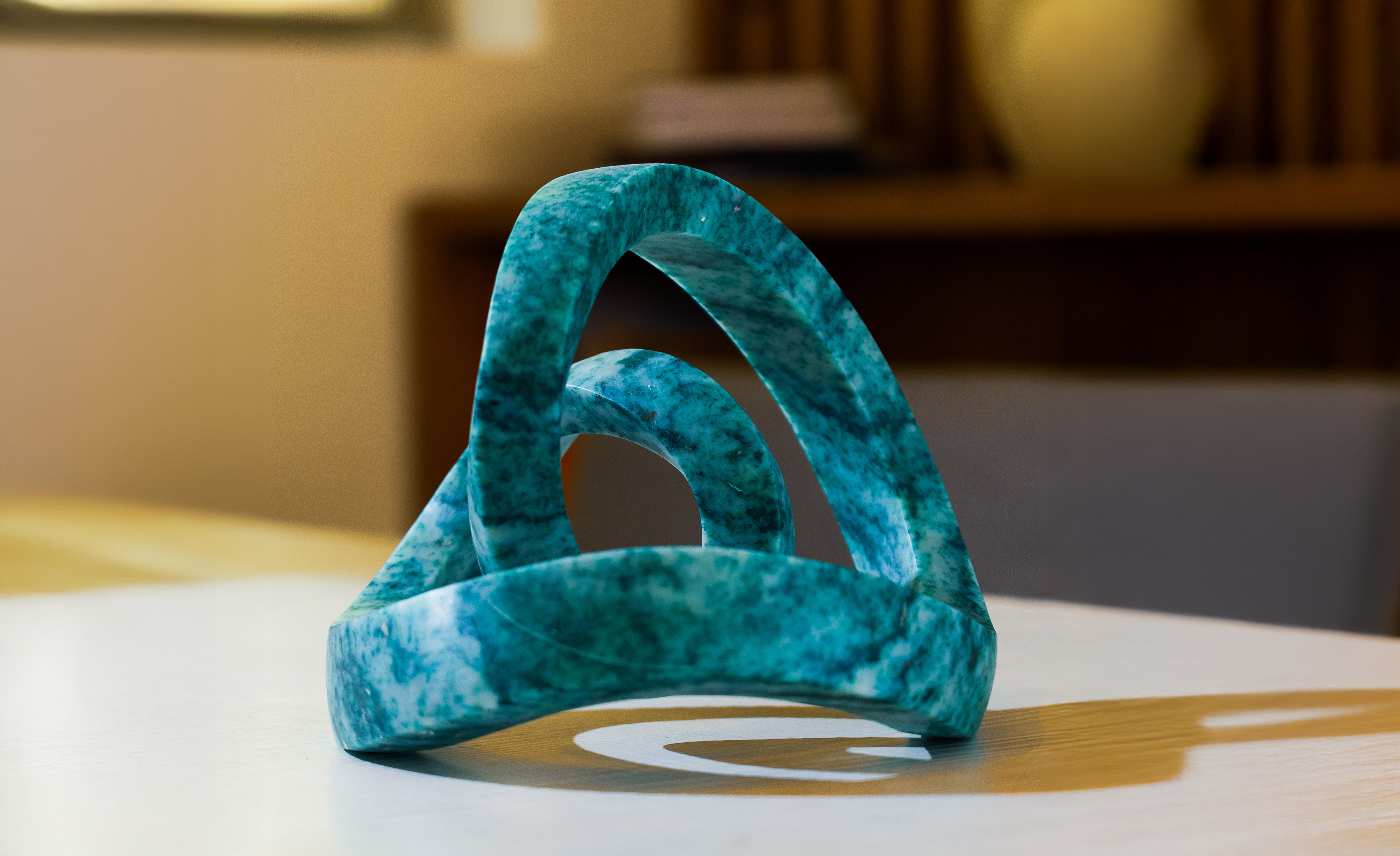 Mottled teal stone sculpture with continuous loops, modern abstract design.