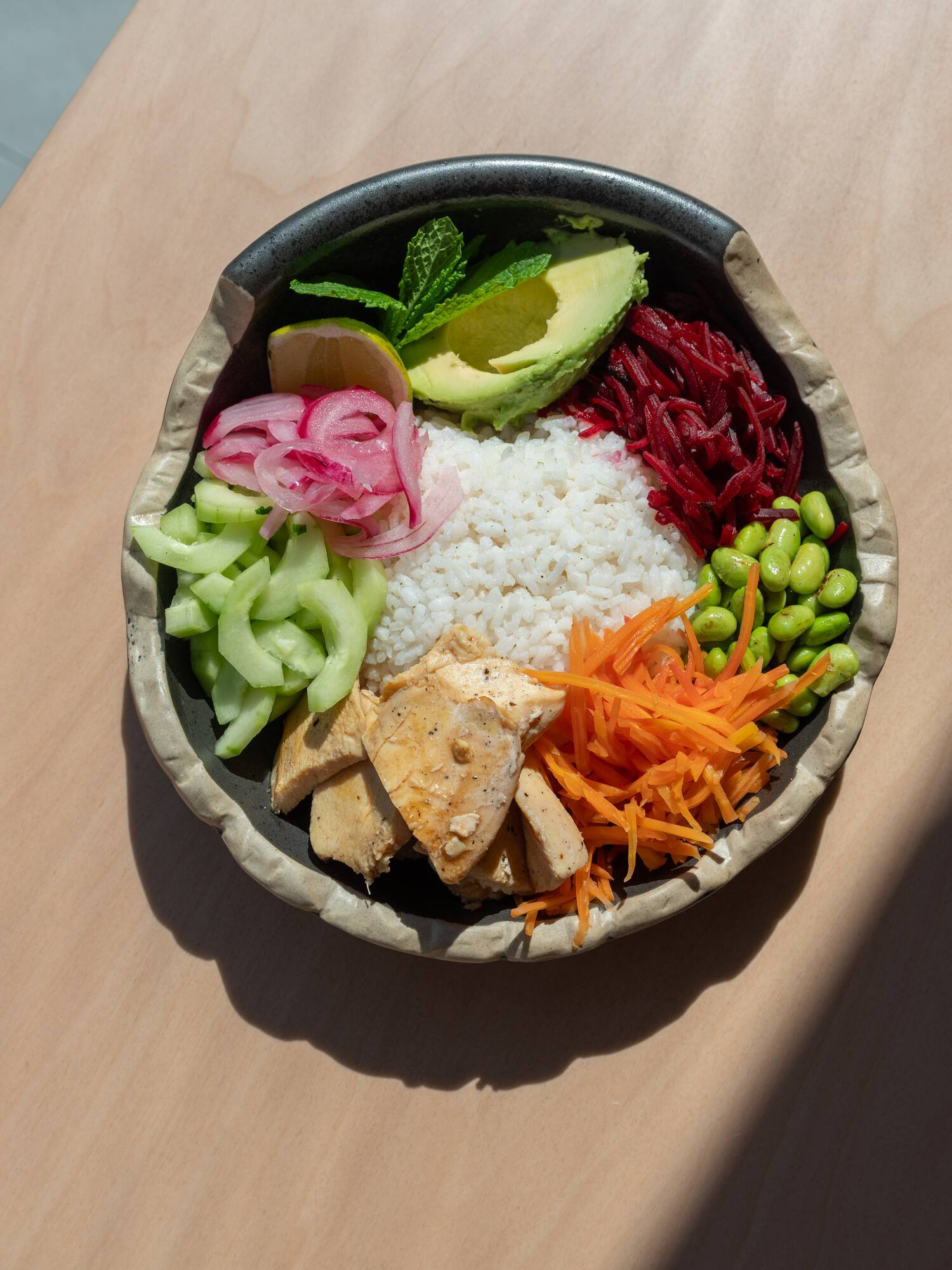 Healthy chicken bowl with rice, avocado, edamame, beets, and pickled onions.