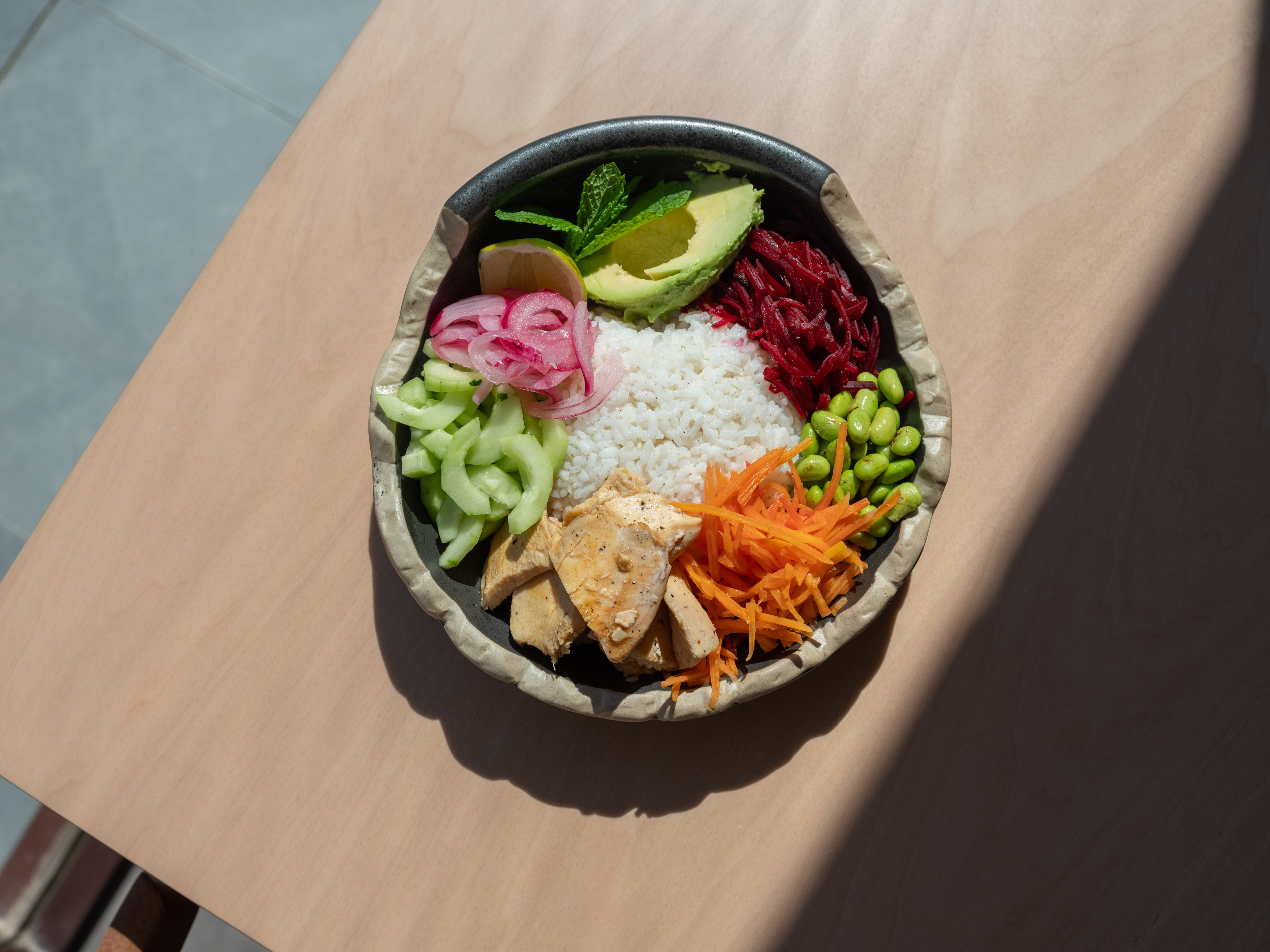 Healthy chicken bowl with rice, avocado, edamame, beets, and pickled onions.
