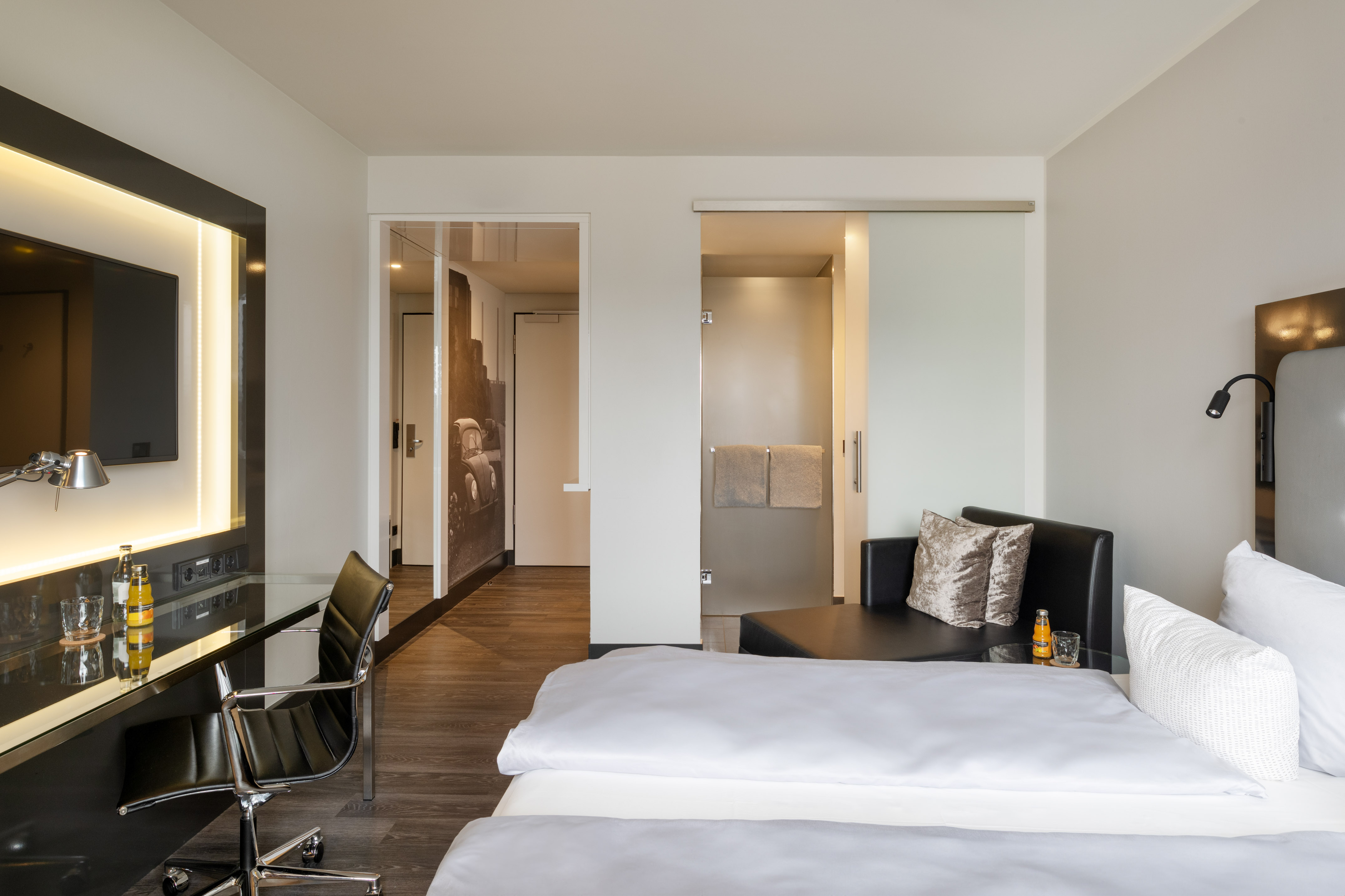 Modern hotel room with bed, desk, TV, and contemporary bathroom access.