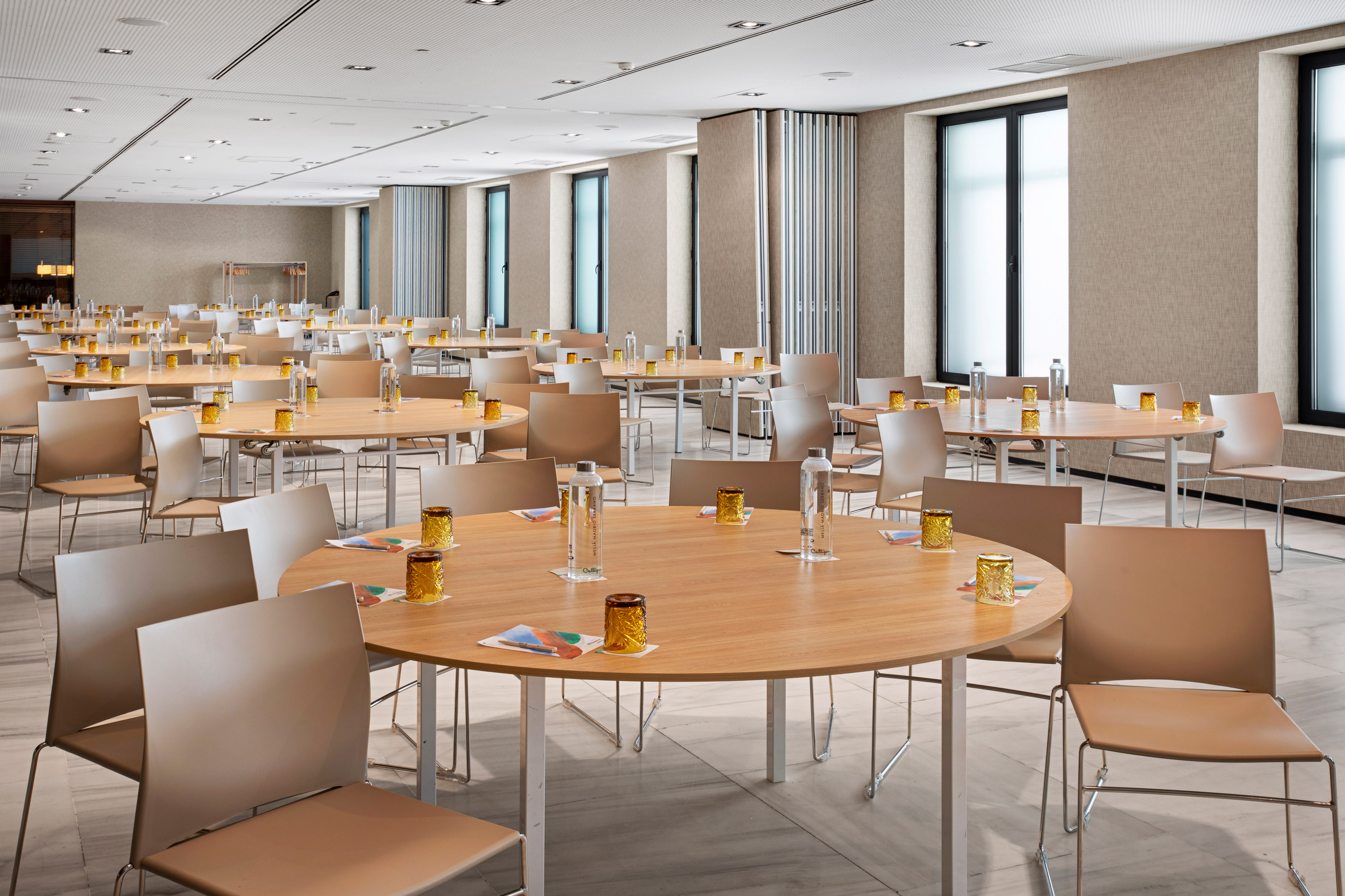 Modern conference room set with round wooden tables and beige chairs.