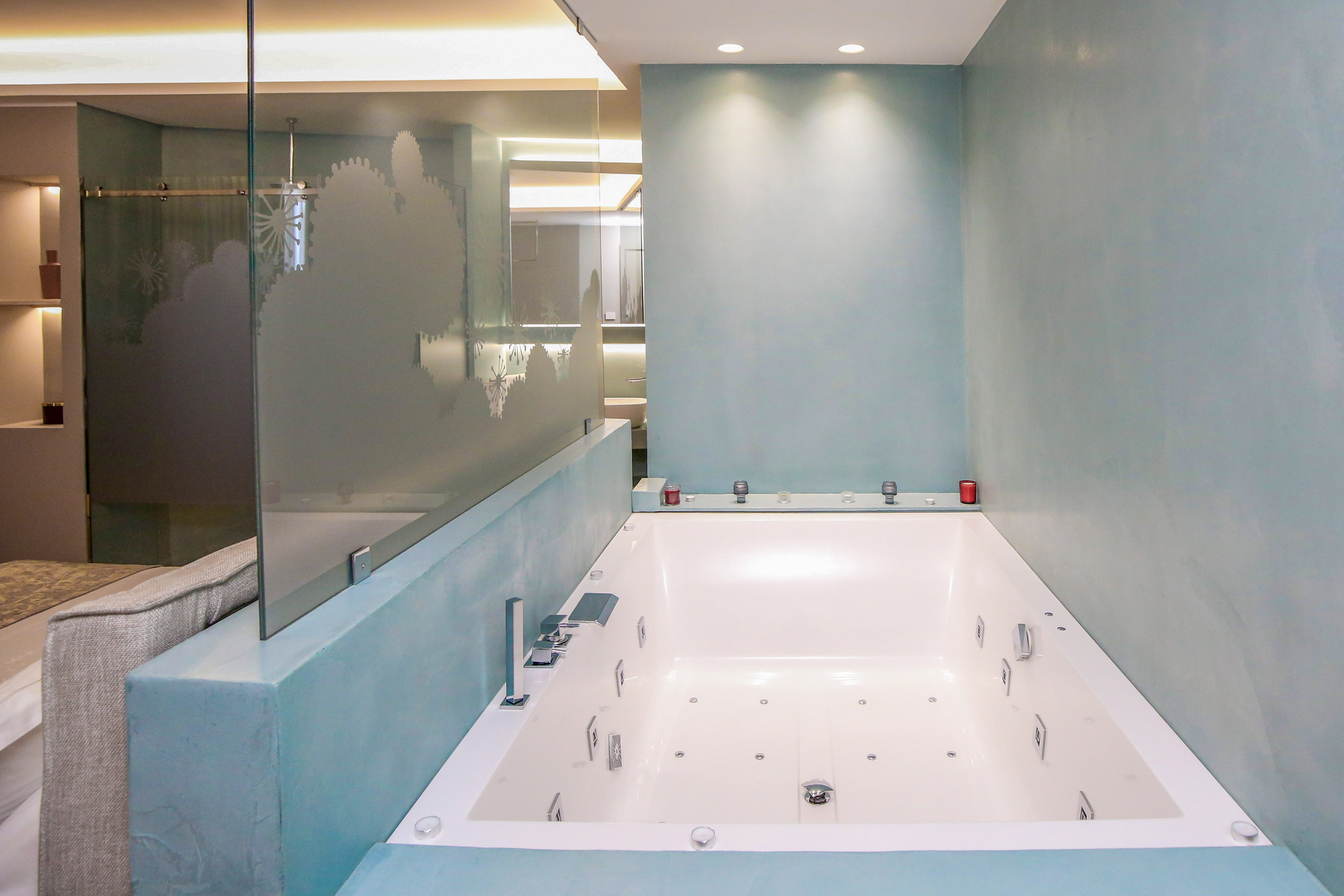 Luxurious white whirlpool tub, light blue modern bathroom with frosted glass.