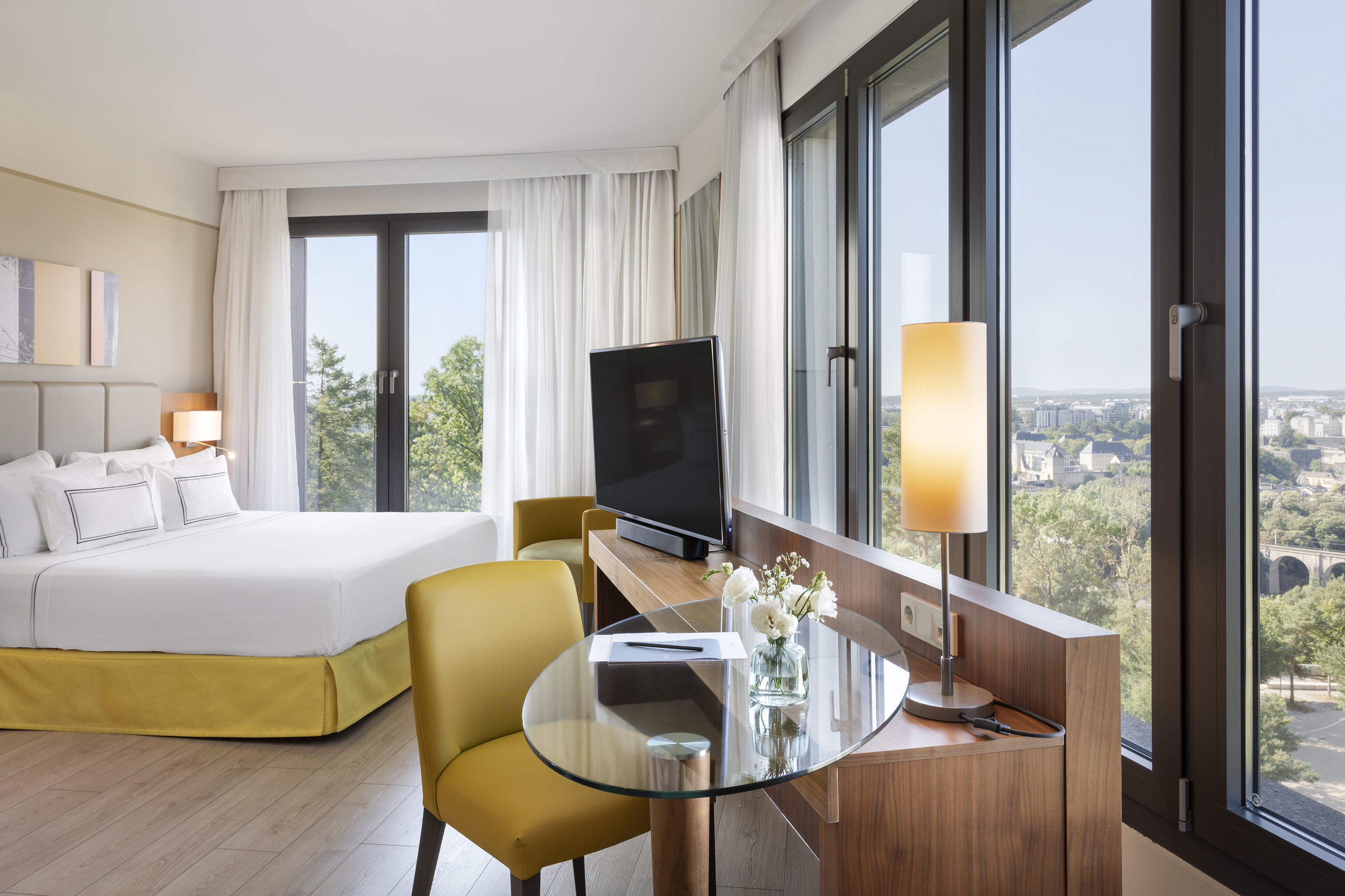 Luxurious hotel suite with city view, large bed, TV, and contemporary decor.