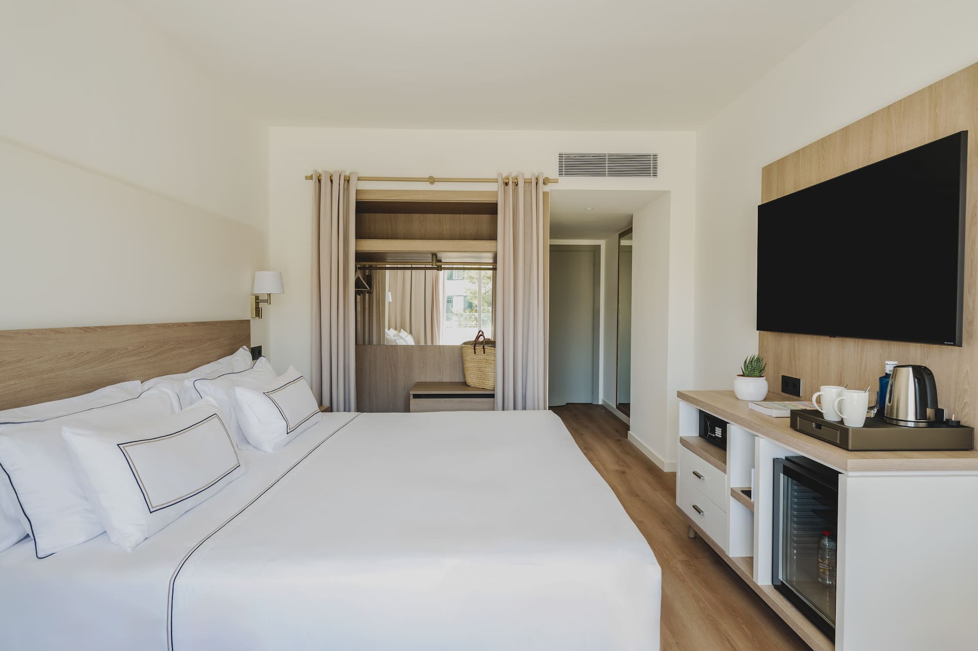 Habitación de hotel moderna con cama king, TV, mini bar y armario.