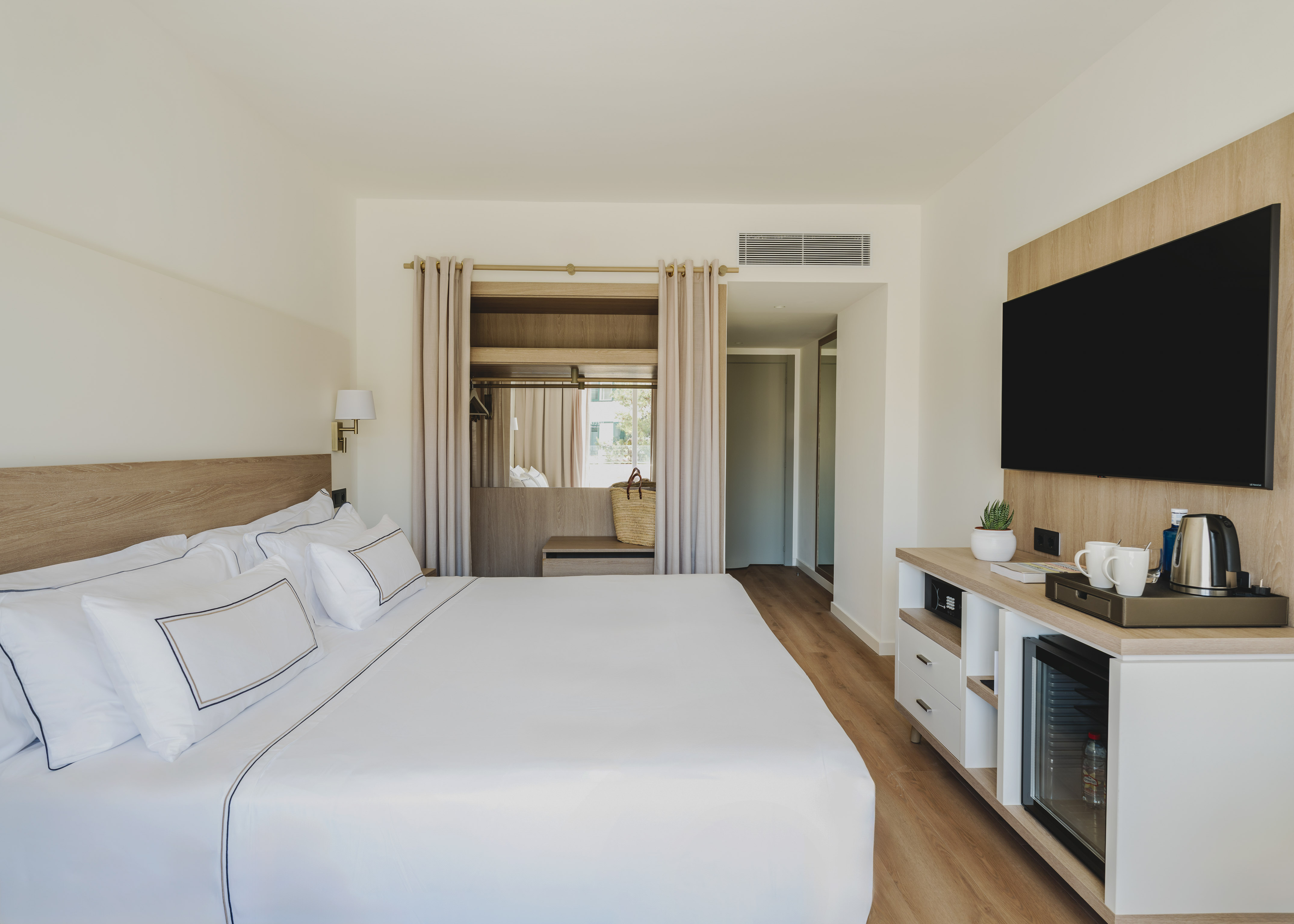 Habitación de hotel moderna con cama king, TV, mini bar y armario.