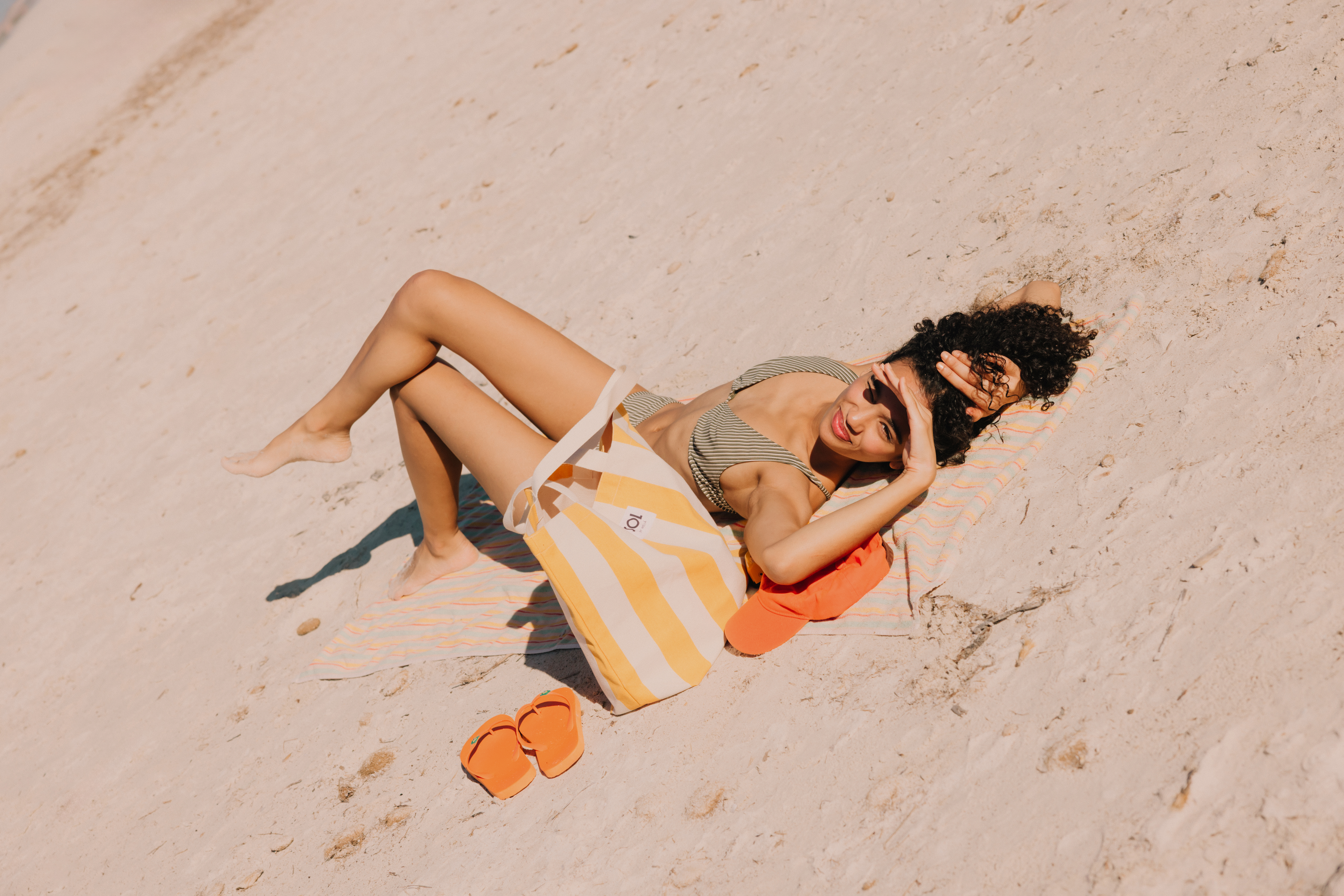 Mujer en bikini a rayas descansando en la playa con bolso y chanclas.