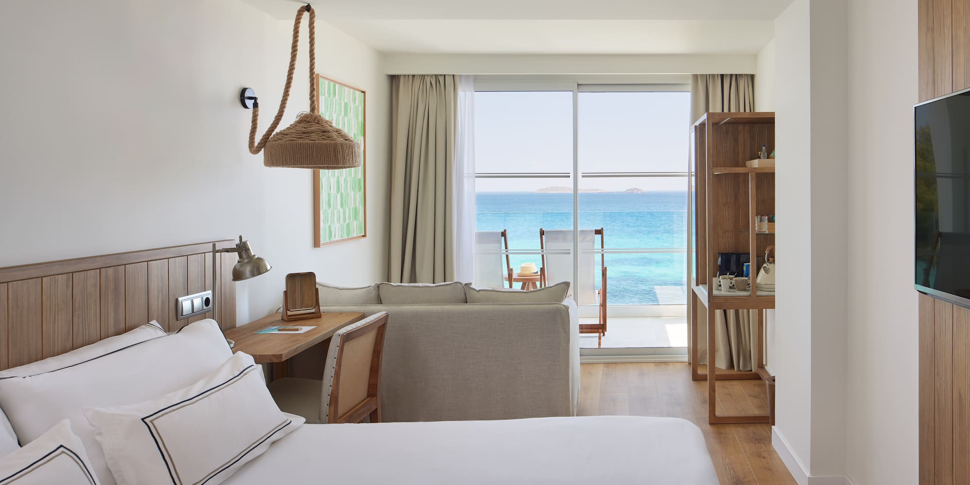 Modern resort room with ocean view balcony, bed, and sofa.