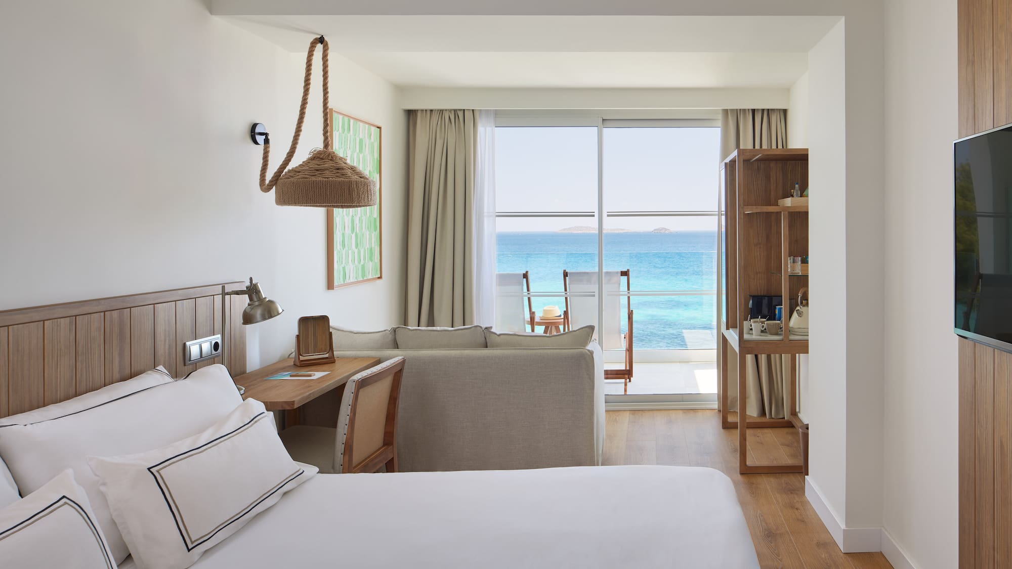 Modern resort room with ocean view balcony, bed, and sofa.