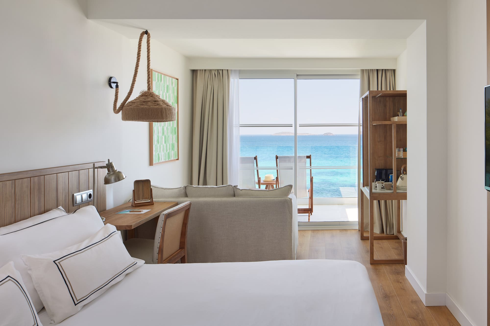 Modern resort room with ocean view balcony, bed, and sofa.