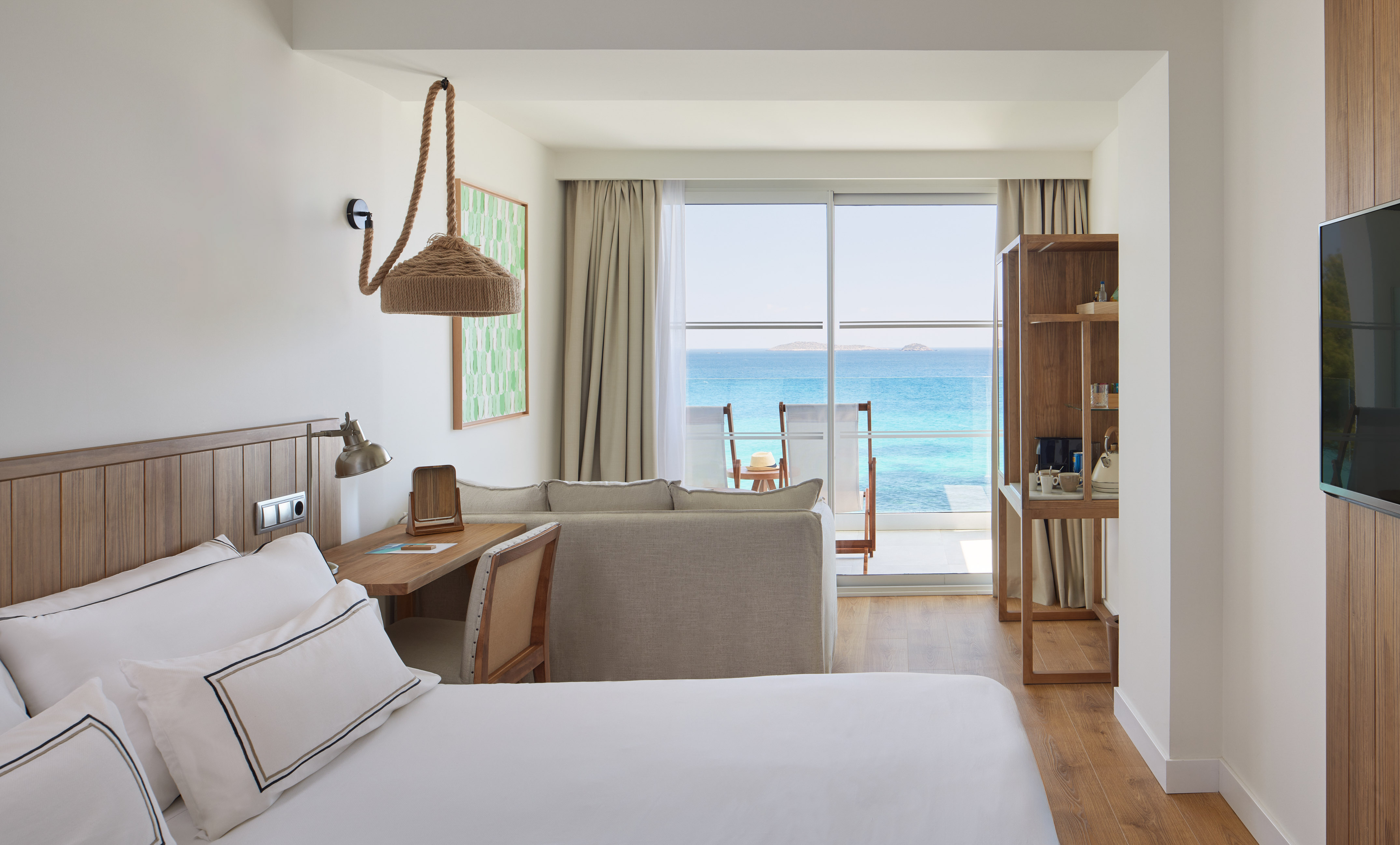 Modern resort room with ocean view balcony, bed, and sofa.