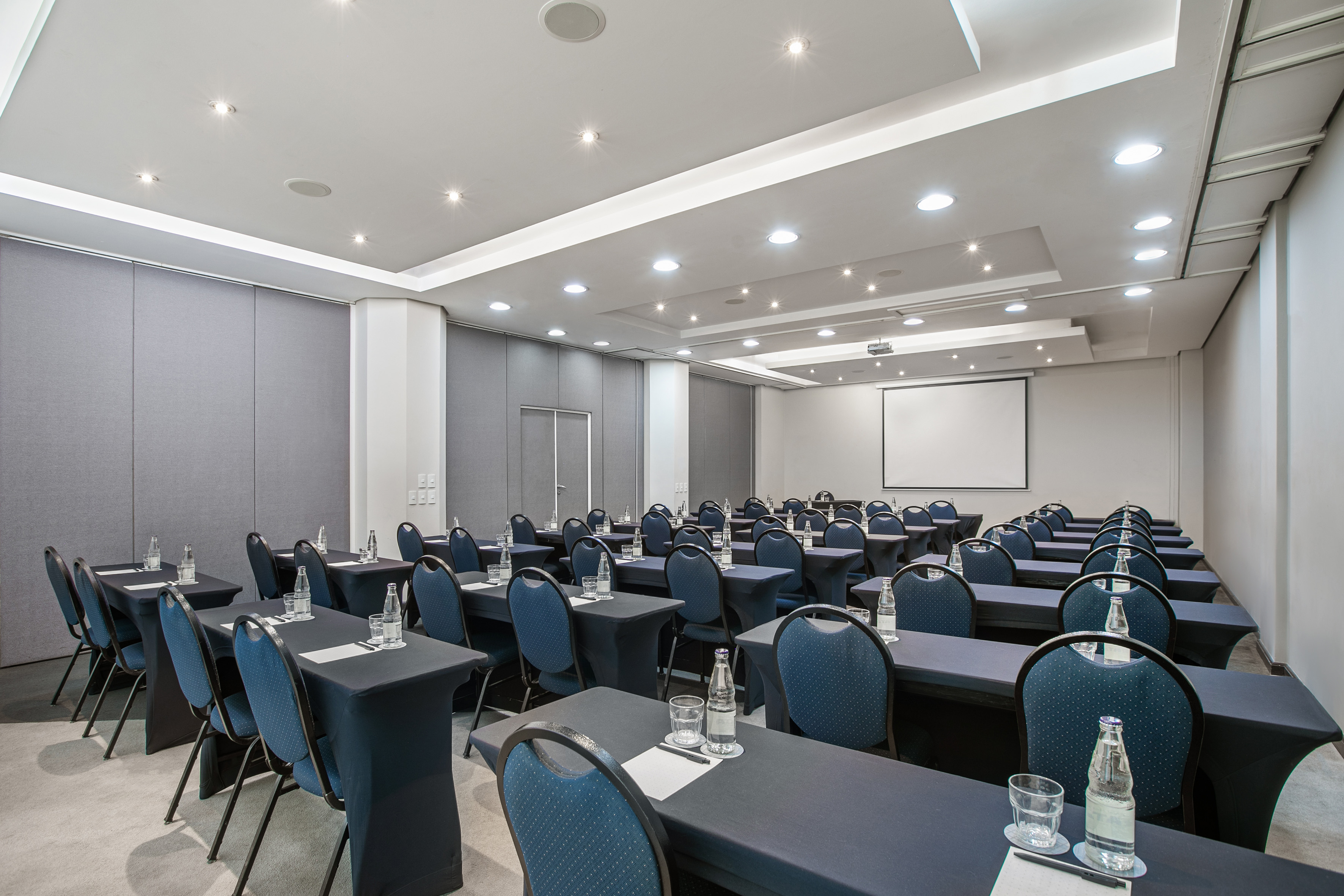Conference room in classroom setup with dark tables, blue chairs, projector screen.