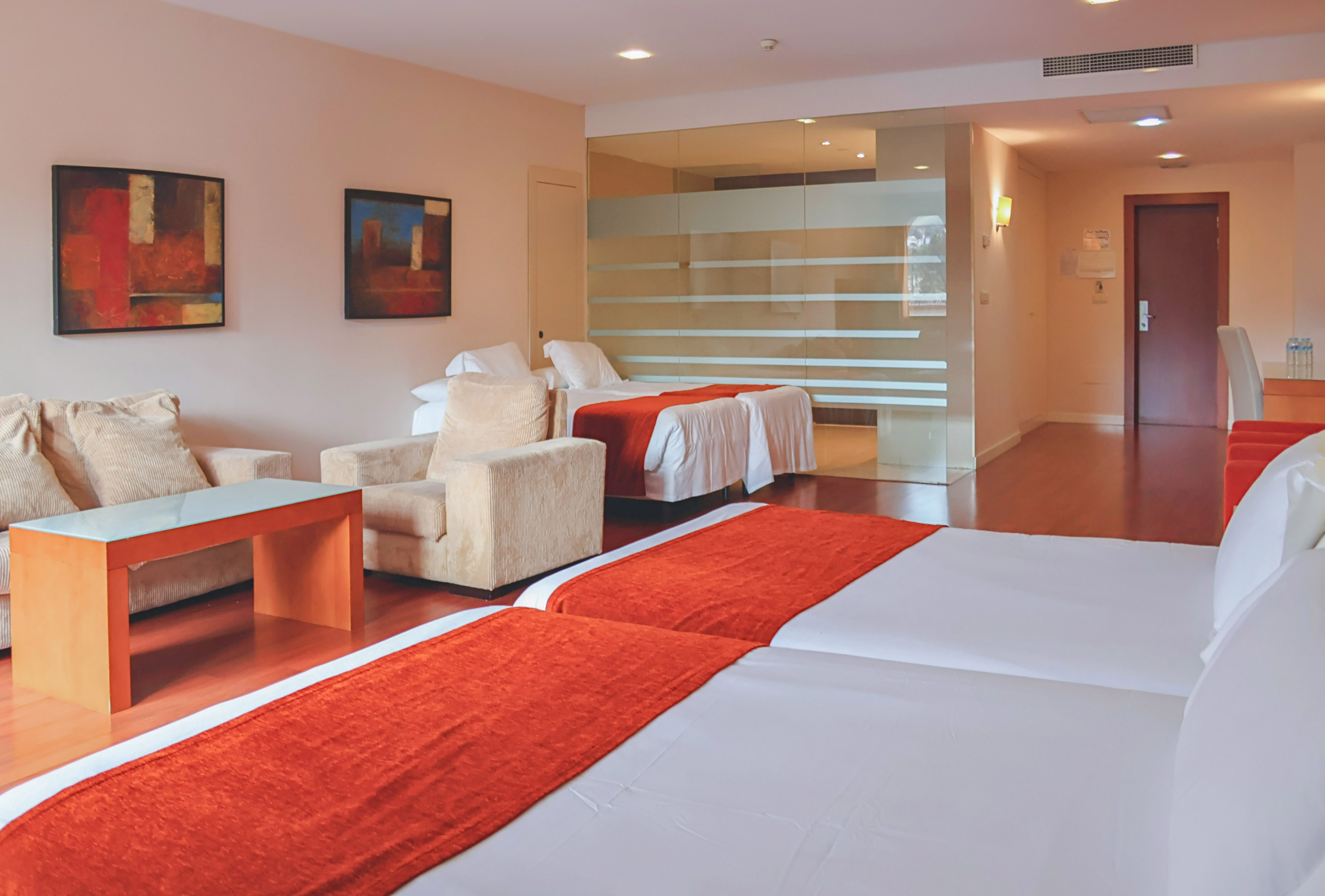 Modern hotel room with two twin beds, sofa, and abstract art.