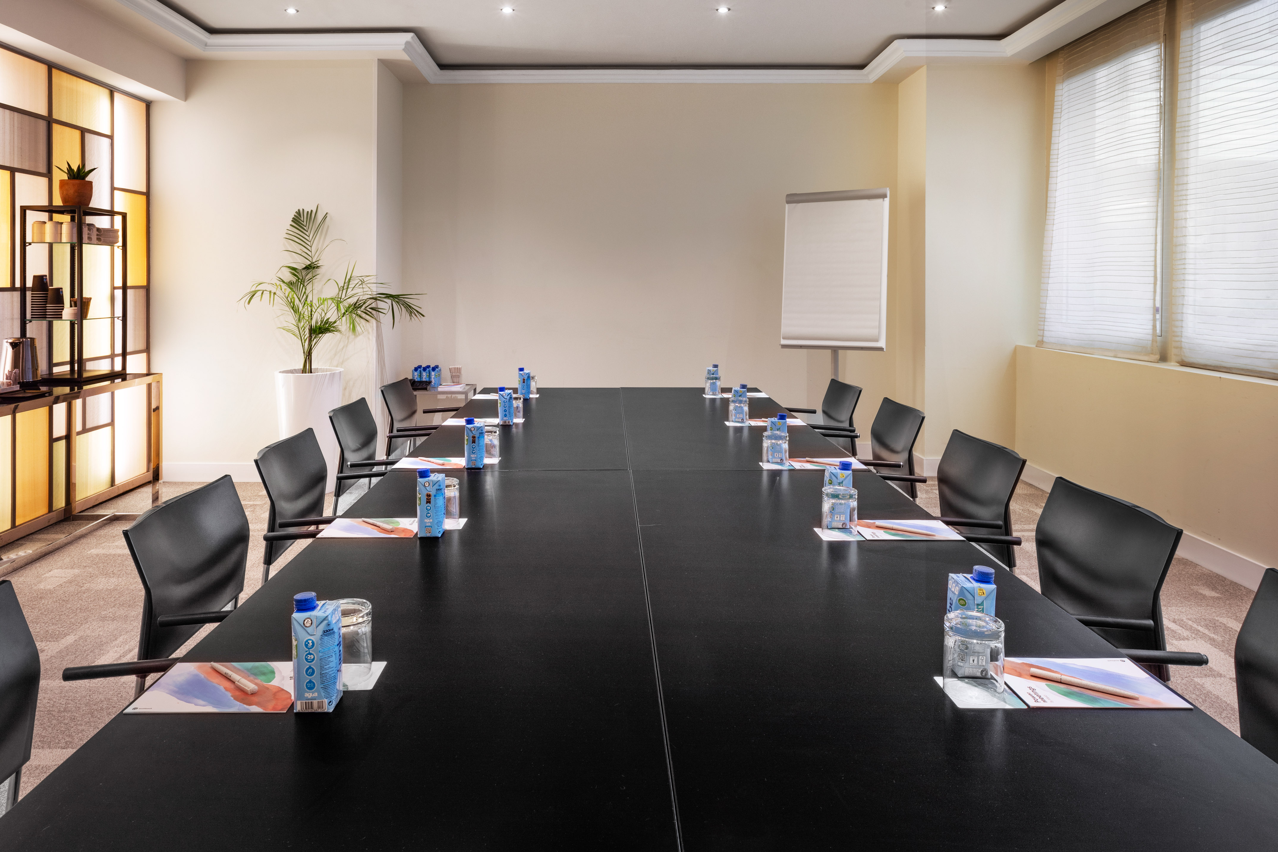 Modern conference room with long table, black chairs, refreshments, and whiteboard.