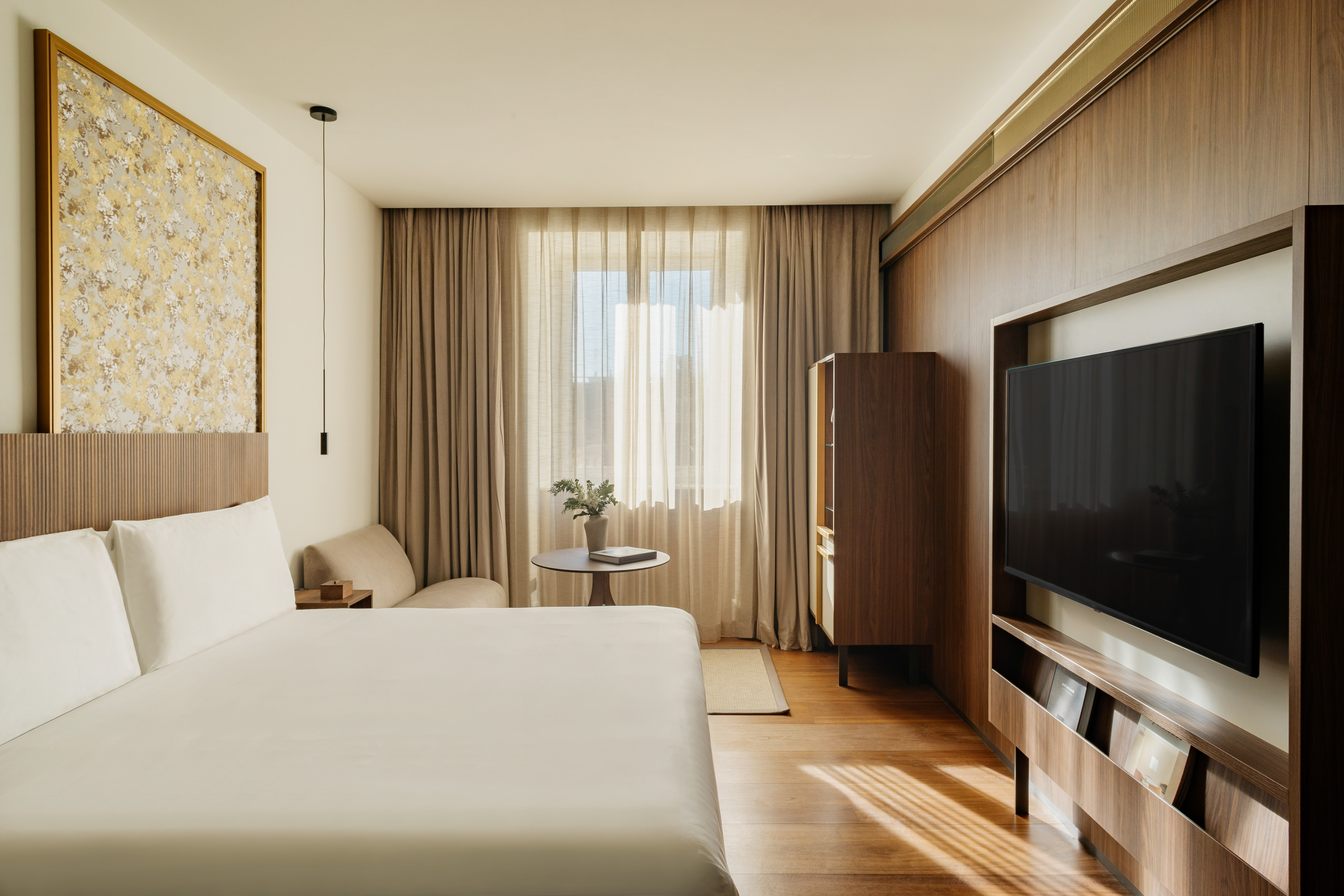 Modern hotel room with king bed, hardwood floors, large window, and wall-mounted TV.