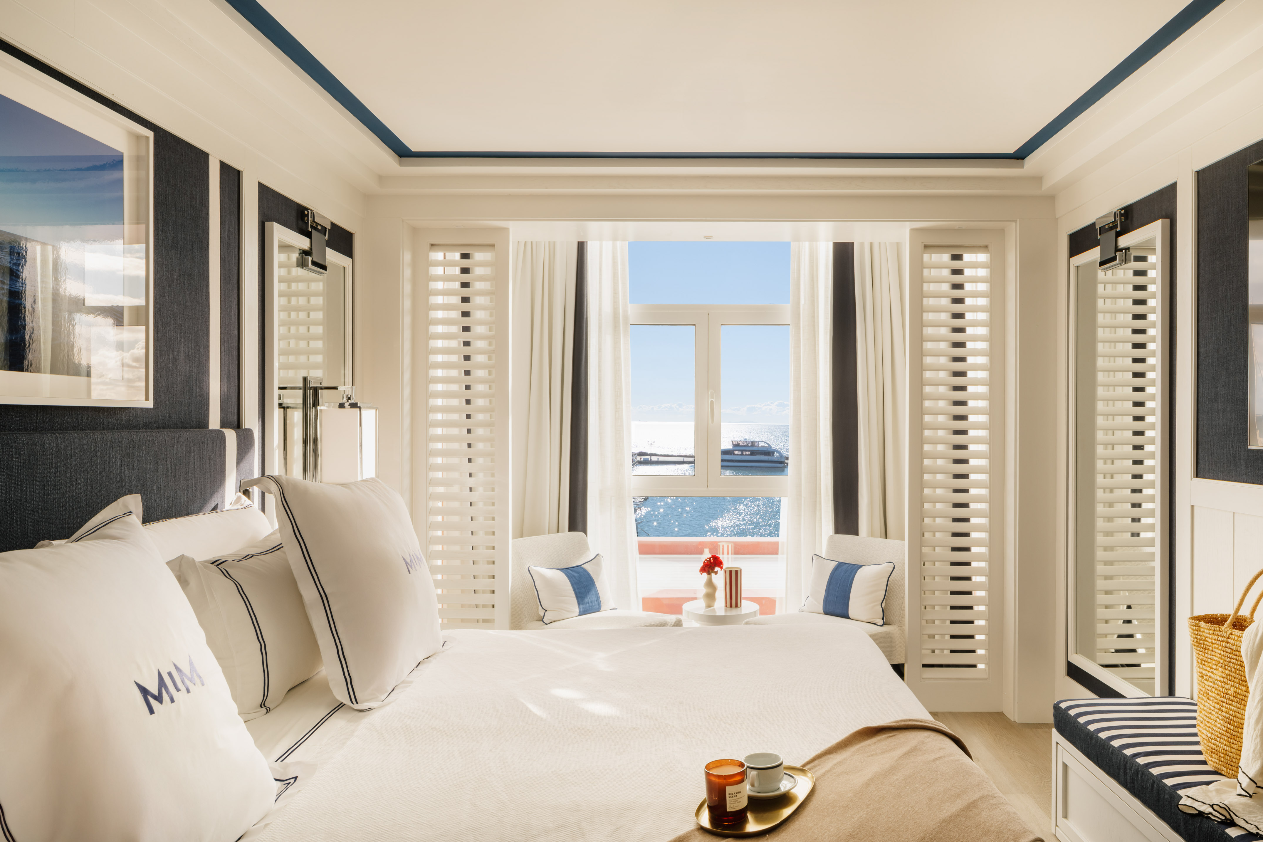 Luxury hotel bedroom with ocean view, white and blue nautical decor.