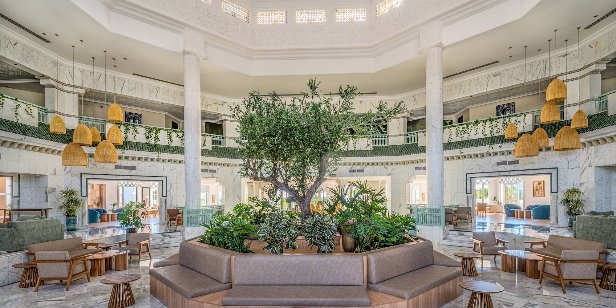Grand hotel lobby with central tree, marble floors, and elegant lounge seating.