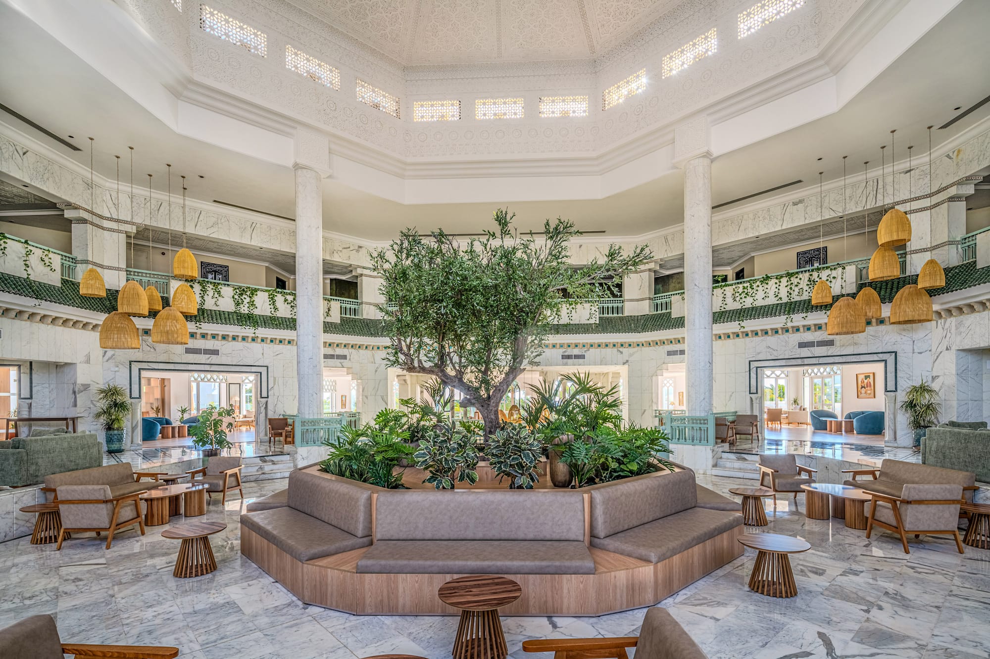 Grand hotel lobby with central tree, marble floors, and elegant lounge seating.
