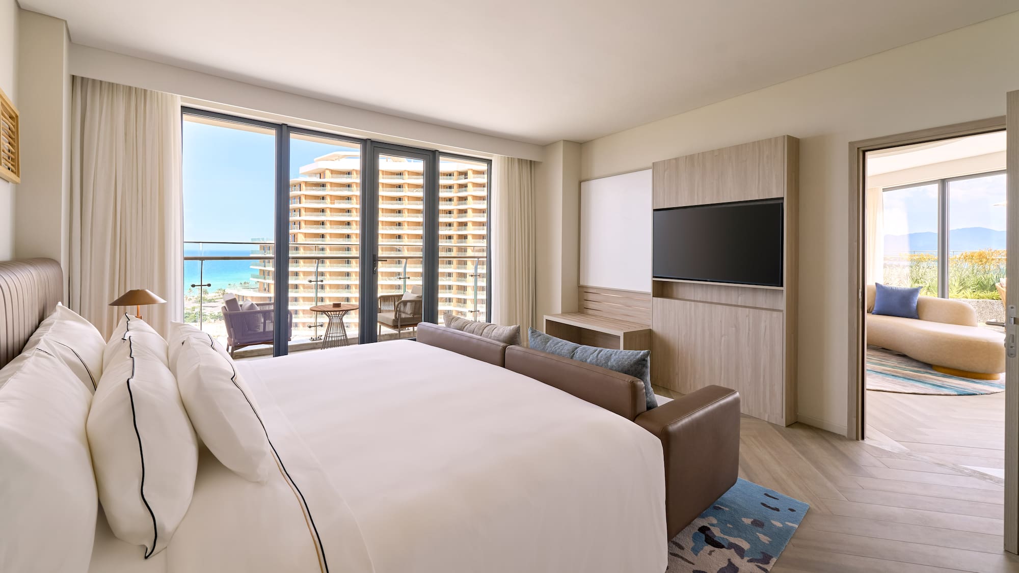 Luxury ocean view hotel suite with king bed and balcony.