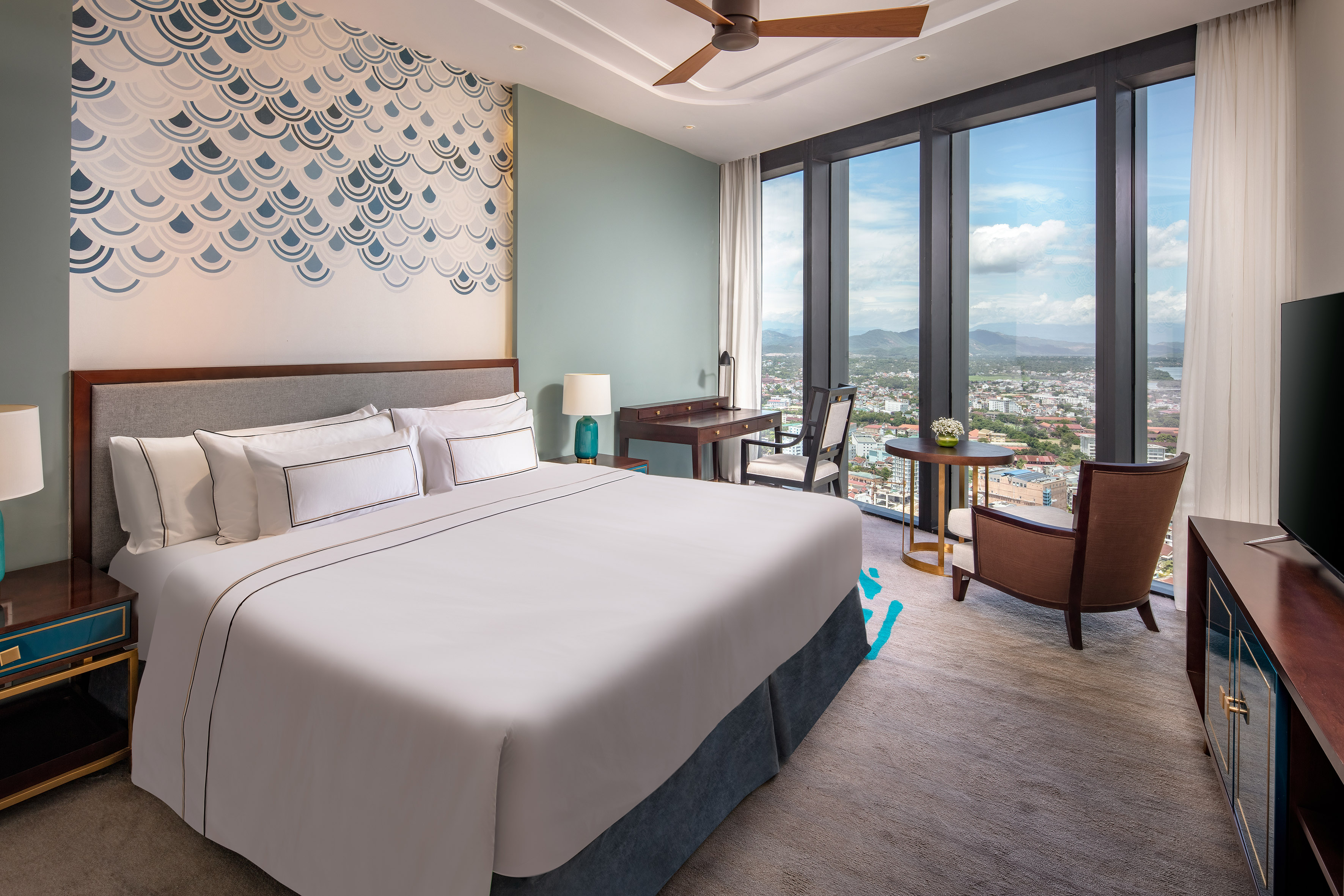 Contemporary hotel room with large bed, wave wall art, and city views.