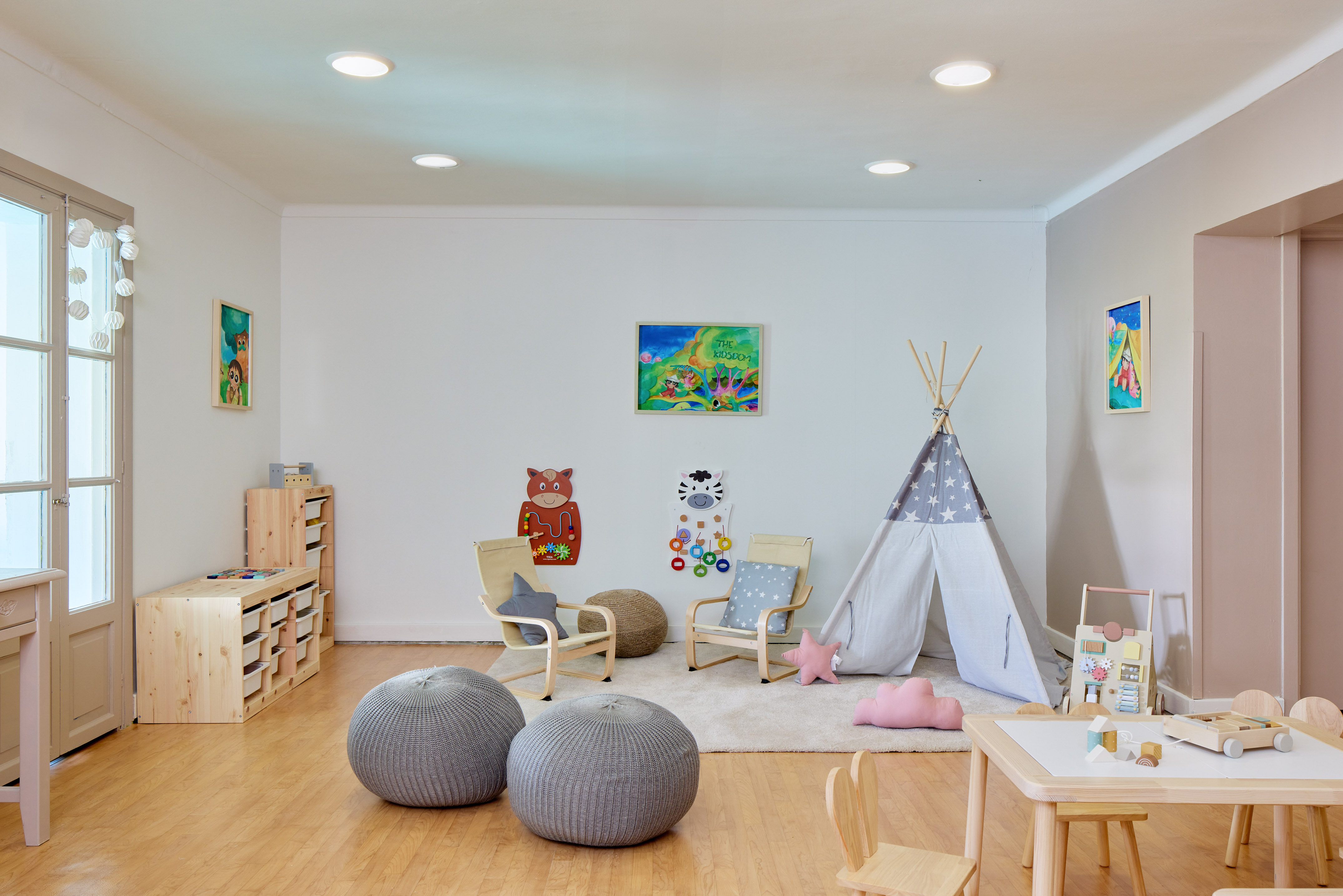 Bright children's playroom with a teepee, wooden furniture, storage, and toys.