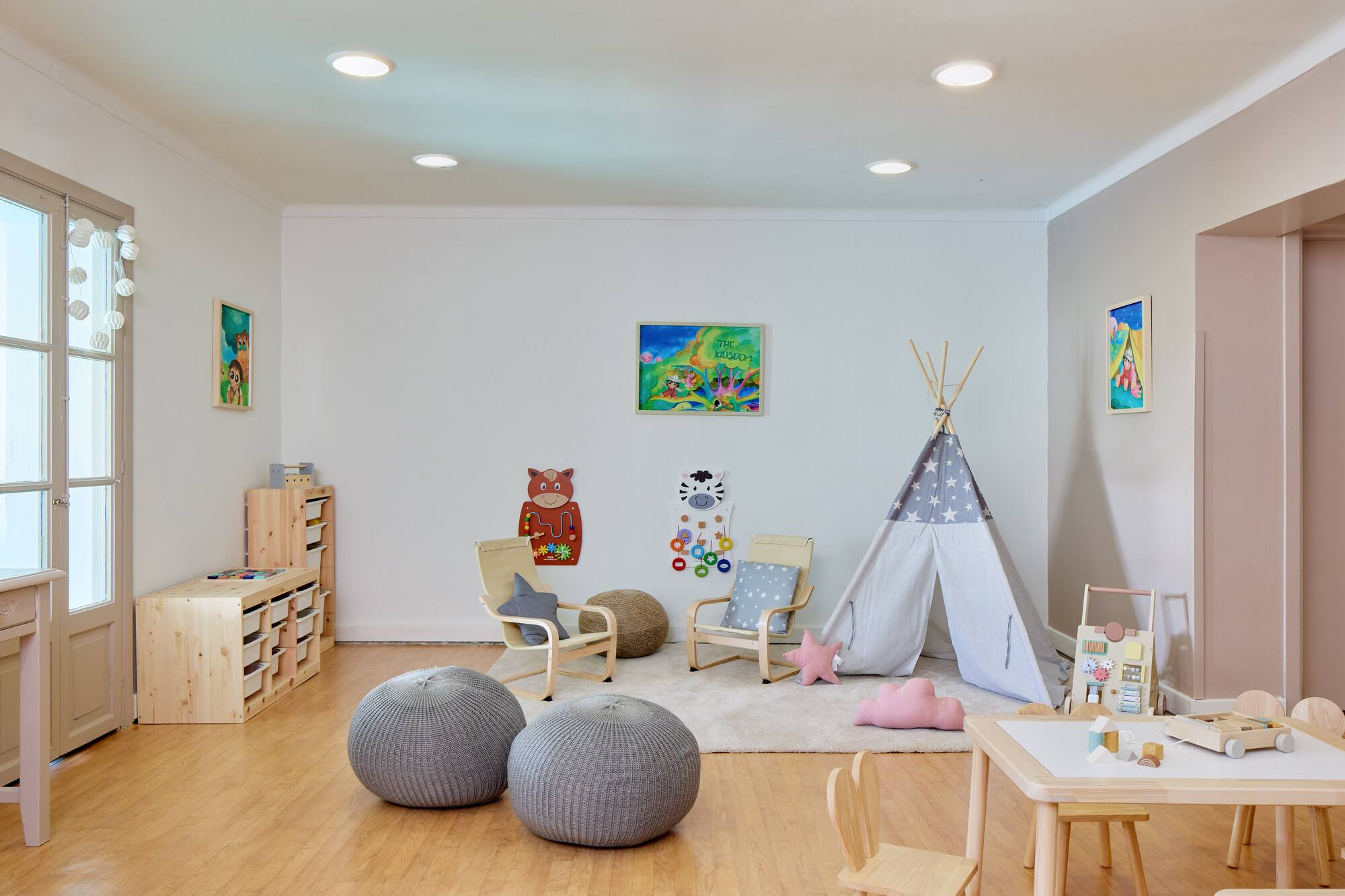 Bright children's playroom with a teepee, wooden furniture, storage, and toys.