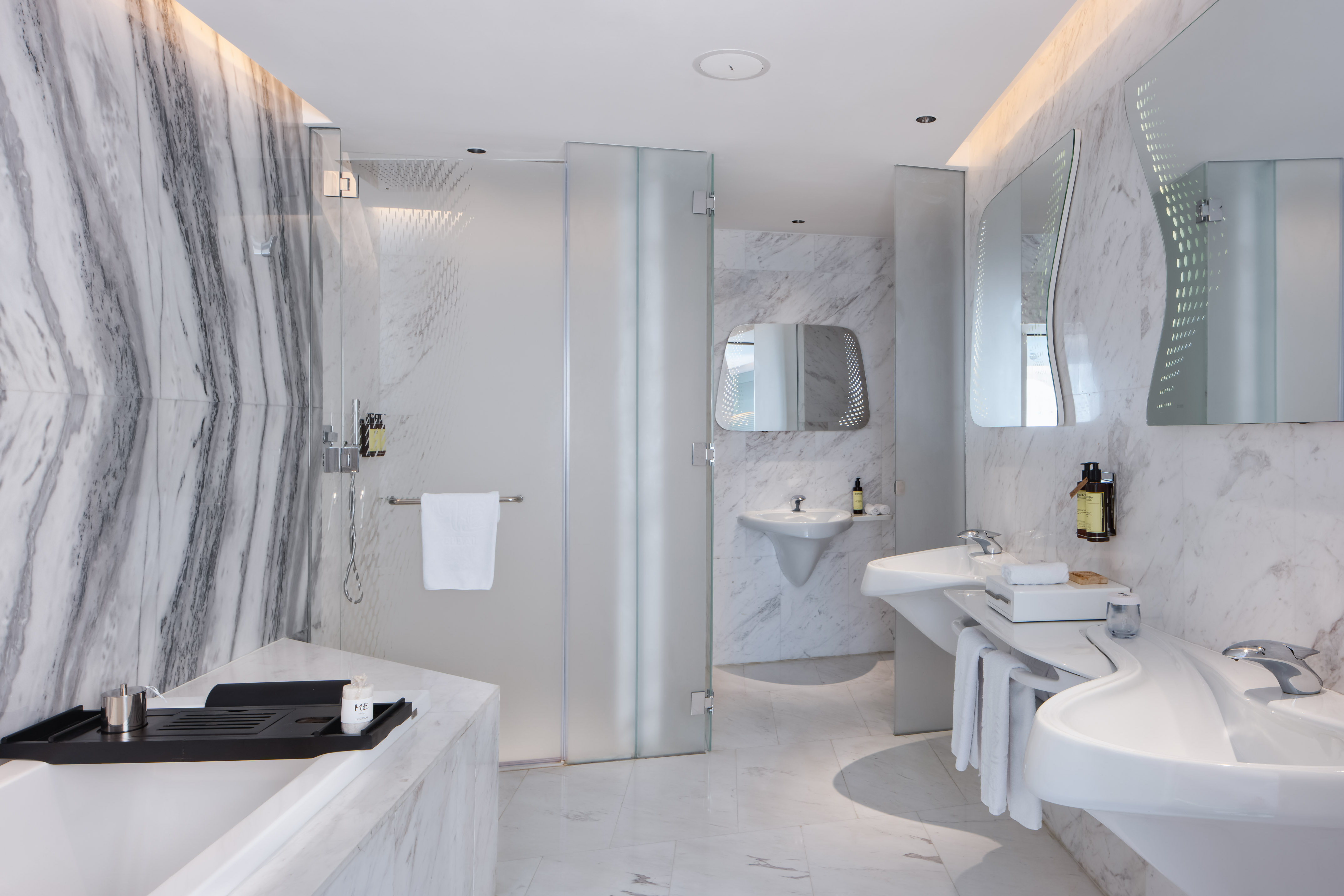 Modern luxury bathroom with marble walls, glass shower, bathtub, and double sinks.