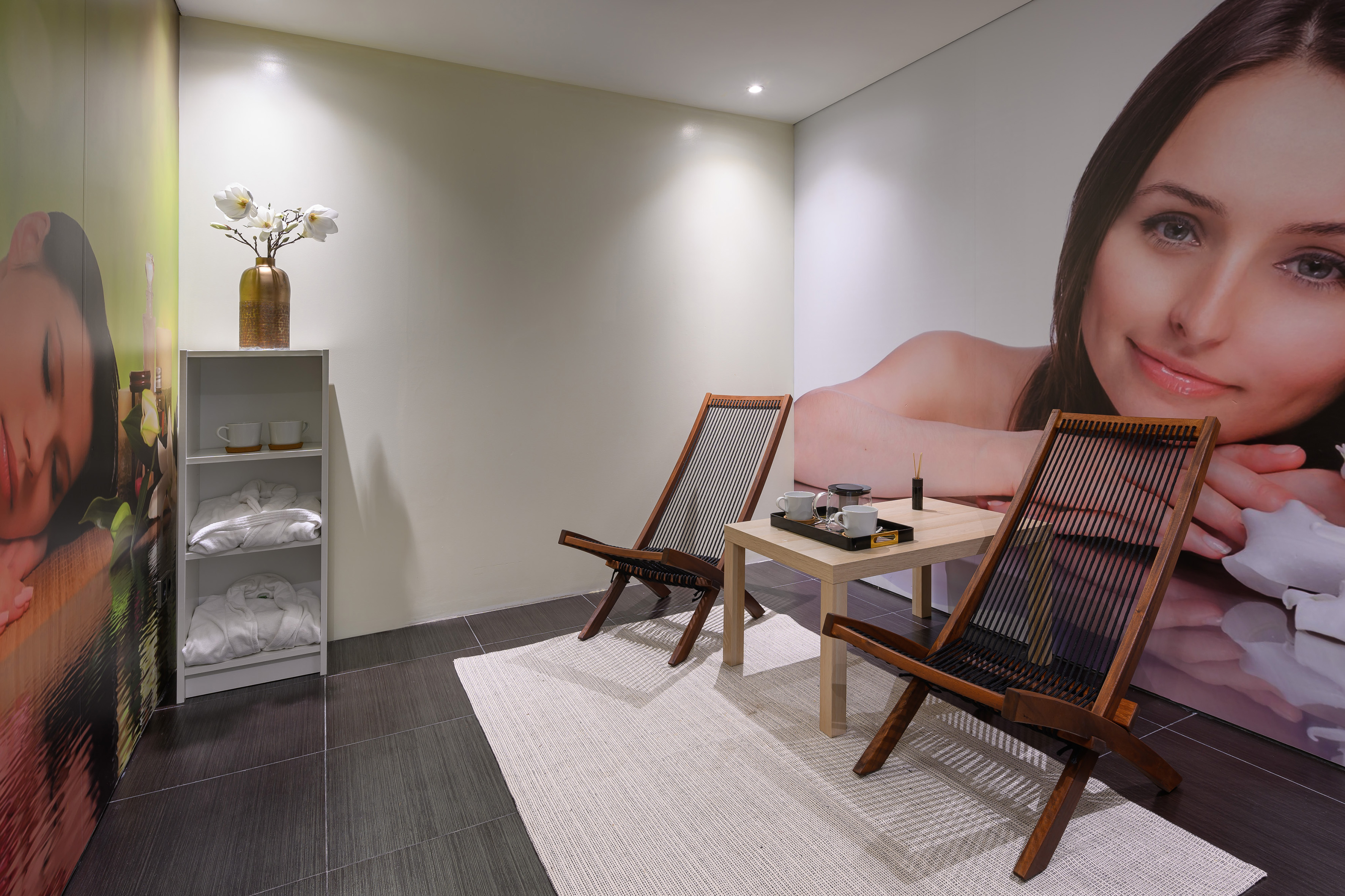 Spa waiting area with lounge chairs, tea station, robes, and large murals.