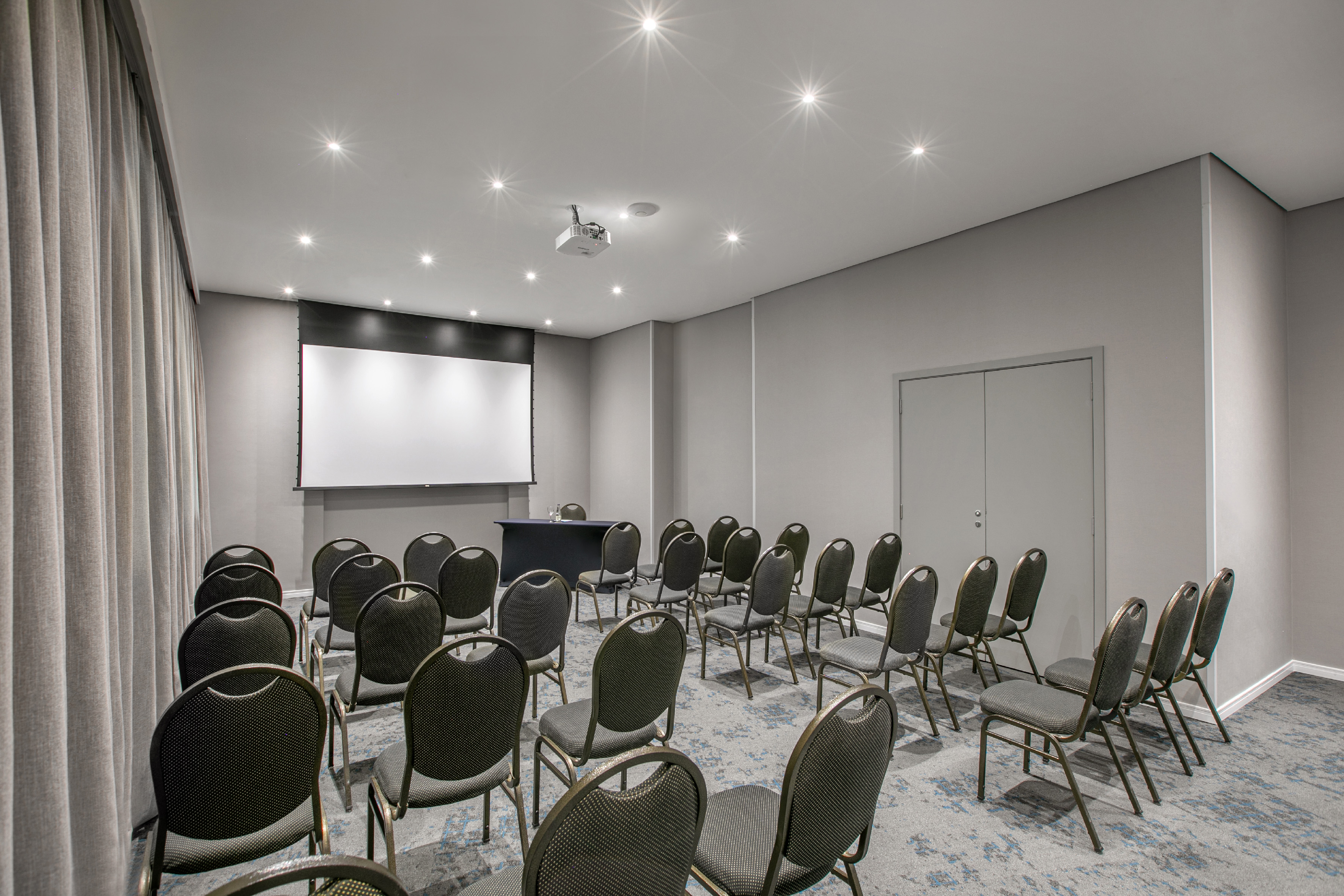 Empty modern meeting room with screen, projector, and grey chairs.