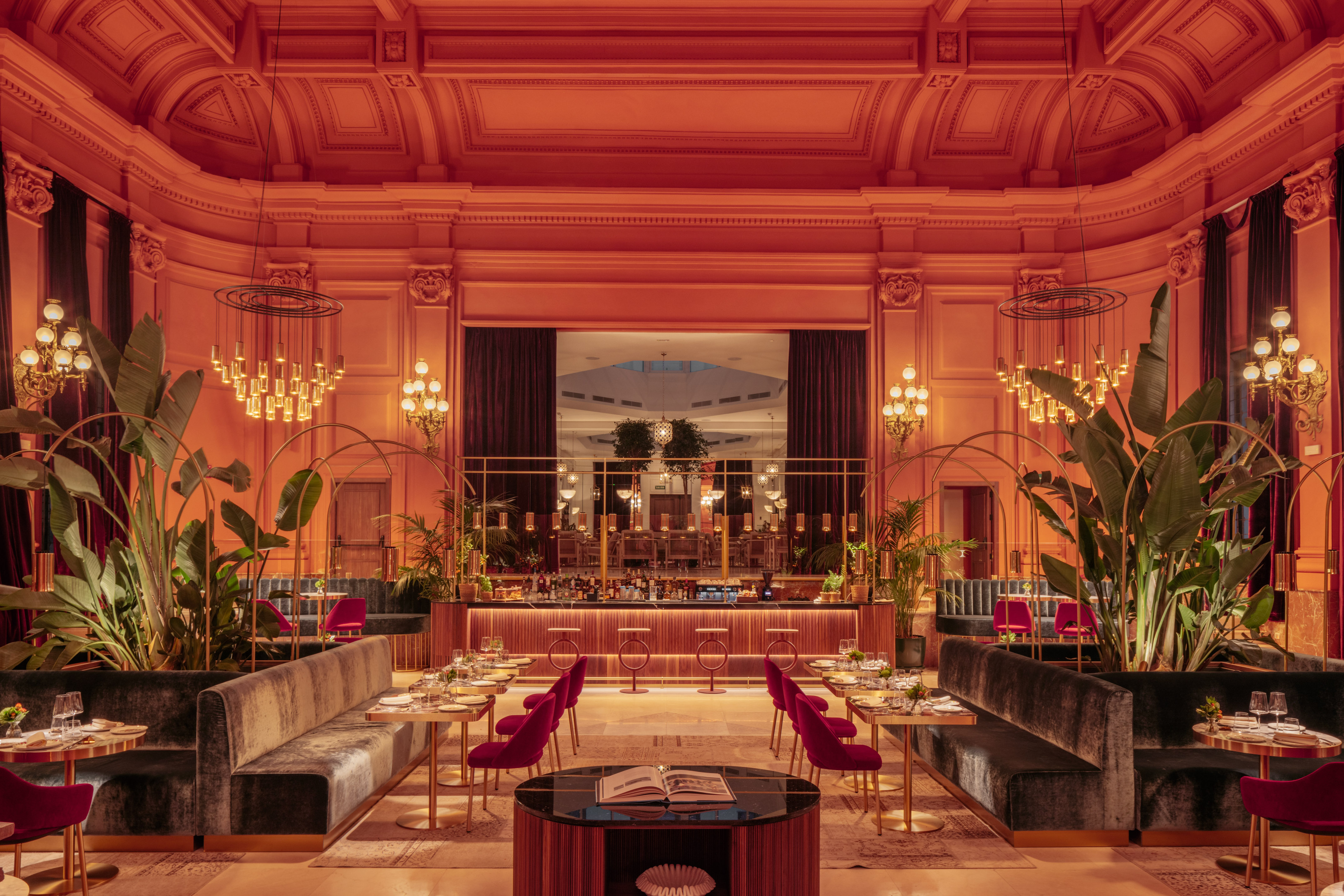Elegant bar and restaurant, warm orange lighting, velvet seating, ornate ceiling.