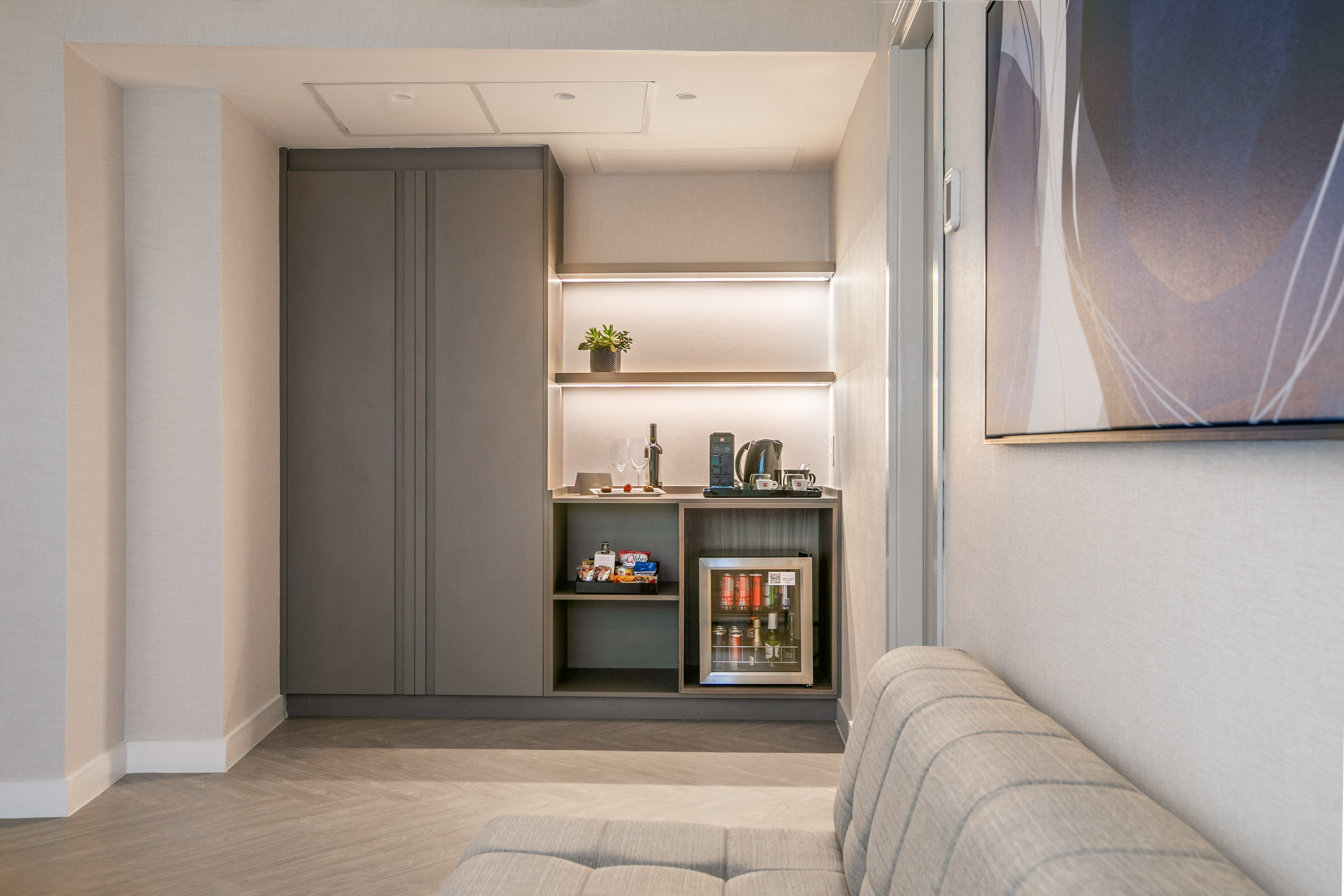 Modern hotel minibar with mini-fridge, coffee station, and snacks.