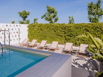 a pool with lounge chairs and a wall with a hedge and a blue sky