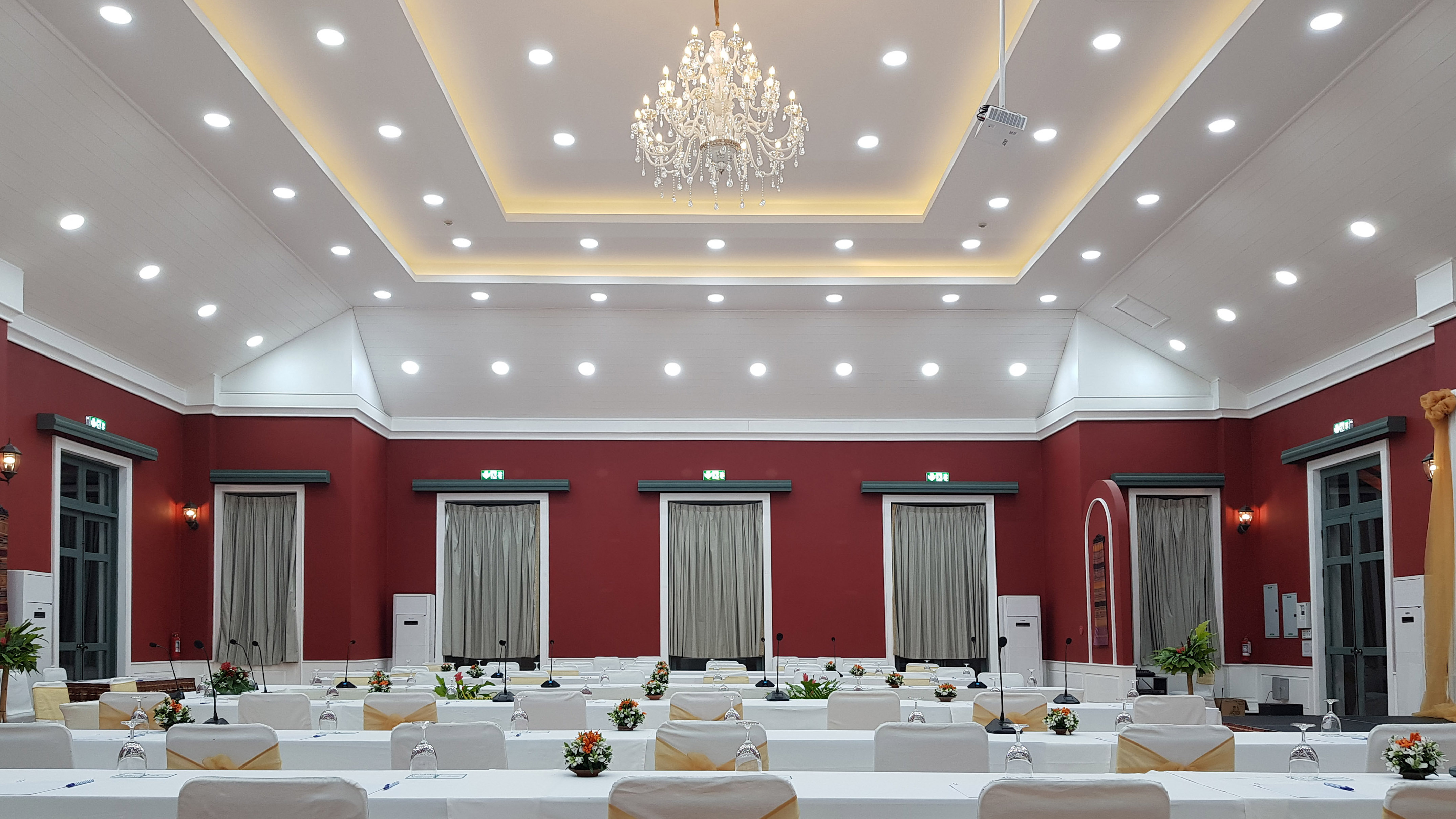 Elegant conference room with red walls, chandelier, and tables set for a meeting.
