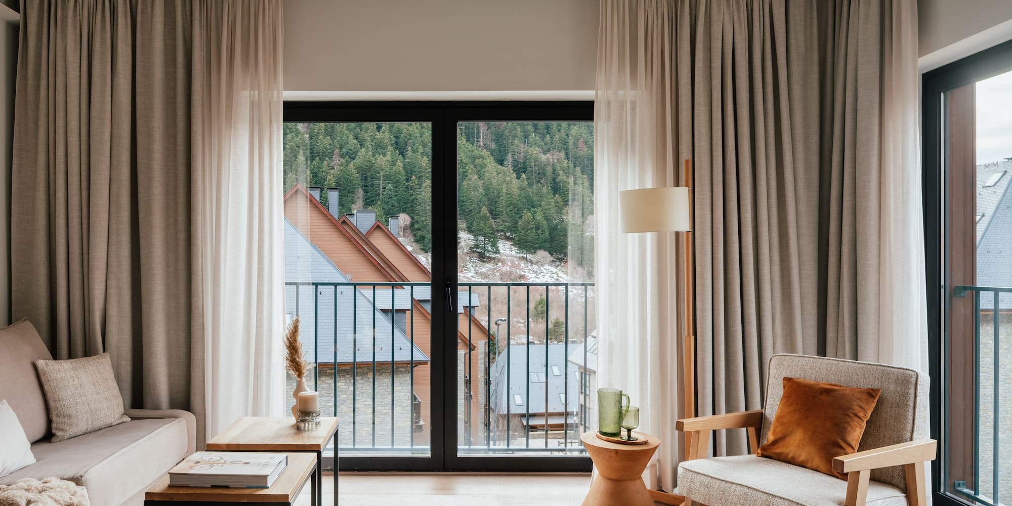 Modern apartment living room with balcony view of mountain forest village.