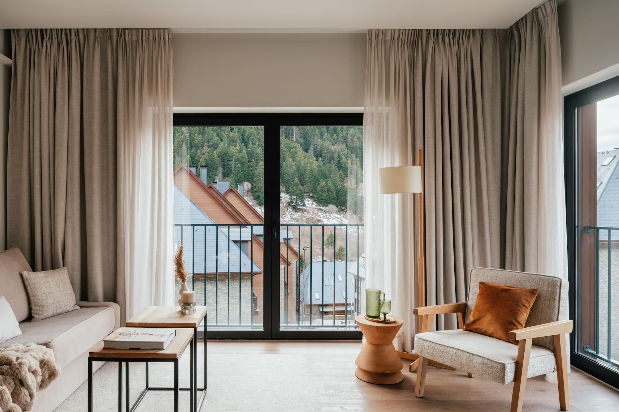 Modern apartment living room with balcony view of mountain forest village.