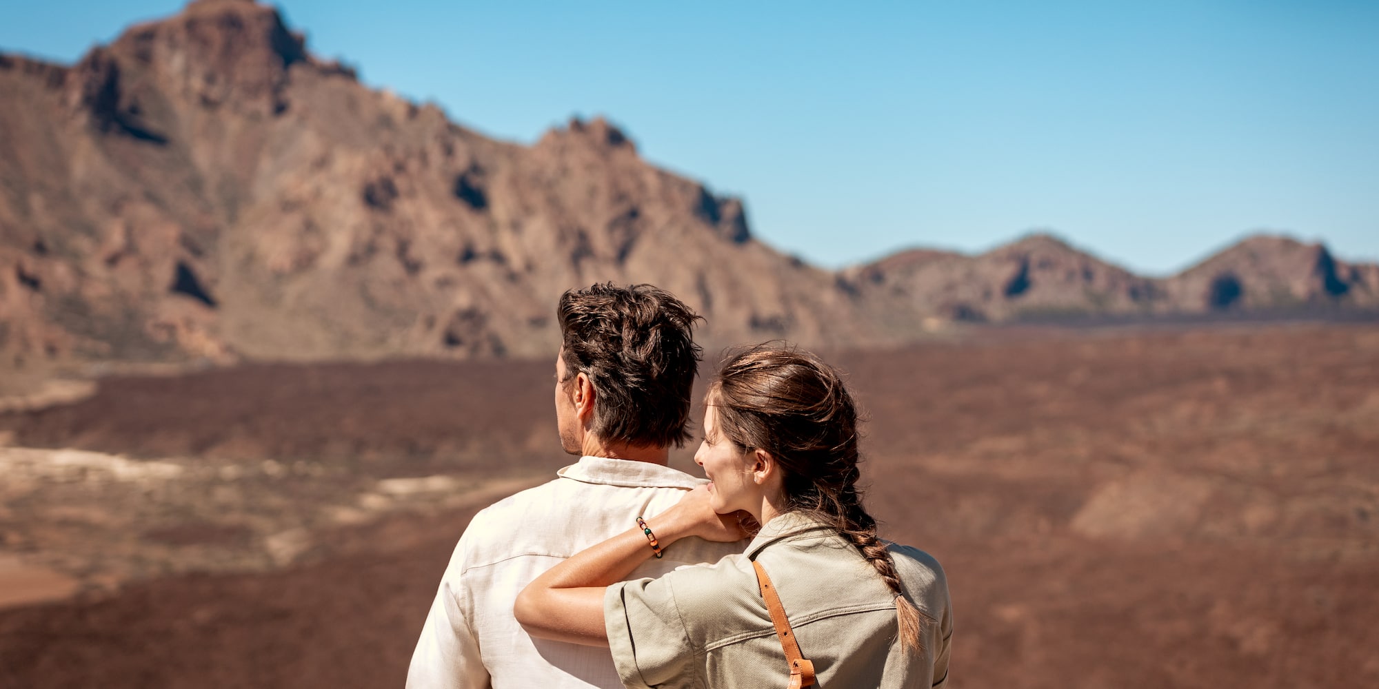 Pareja de espaldas admira paisaje montañoso volcánico. Viaje.