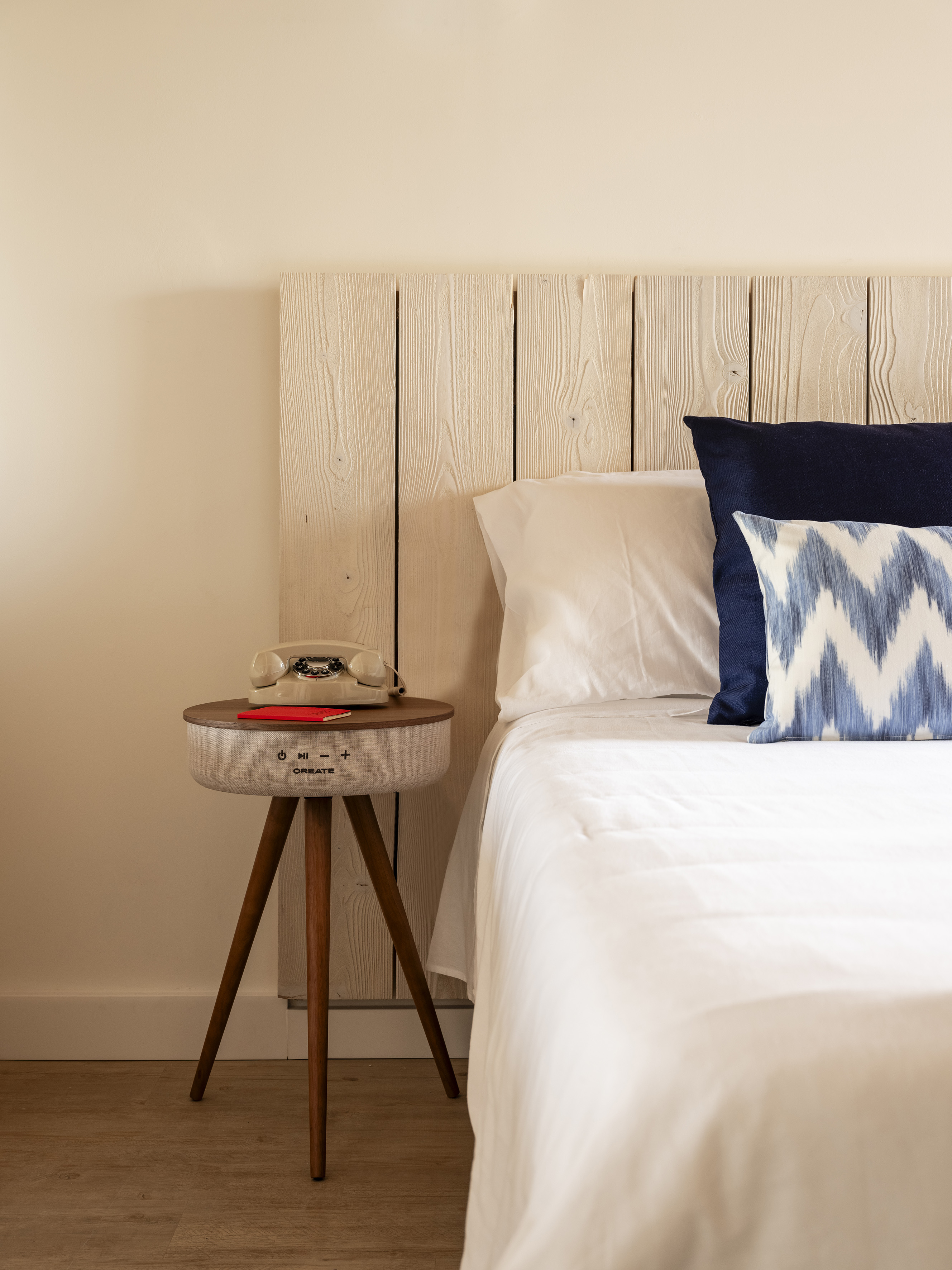 Rustic wood headboard, white bed, speaker nightstand, and vintage phone.