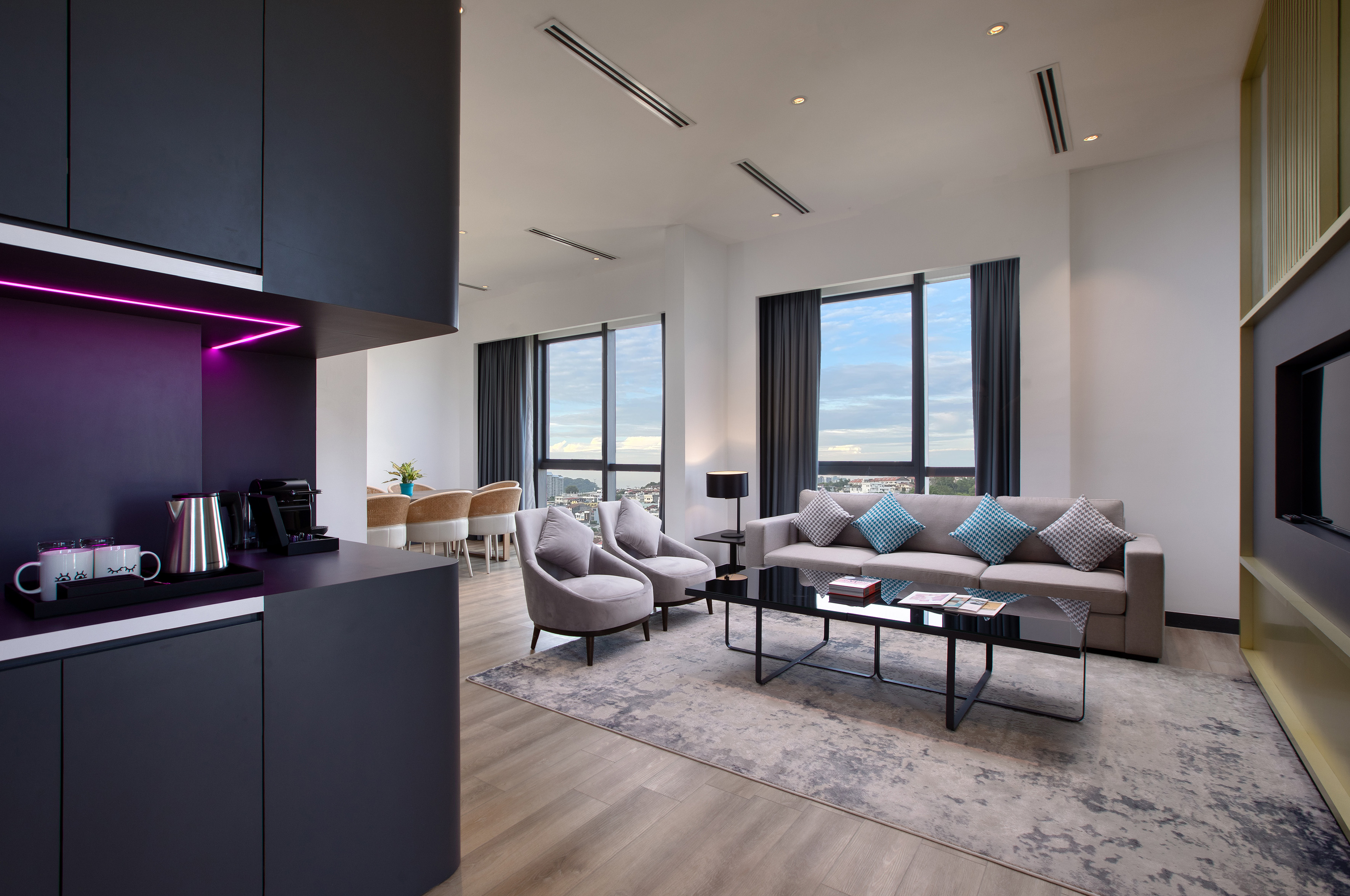 Modern hotel suite living room with city view, kitchenette, and dining area.