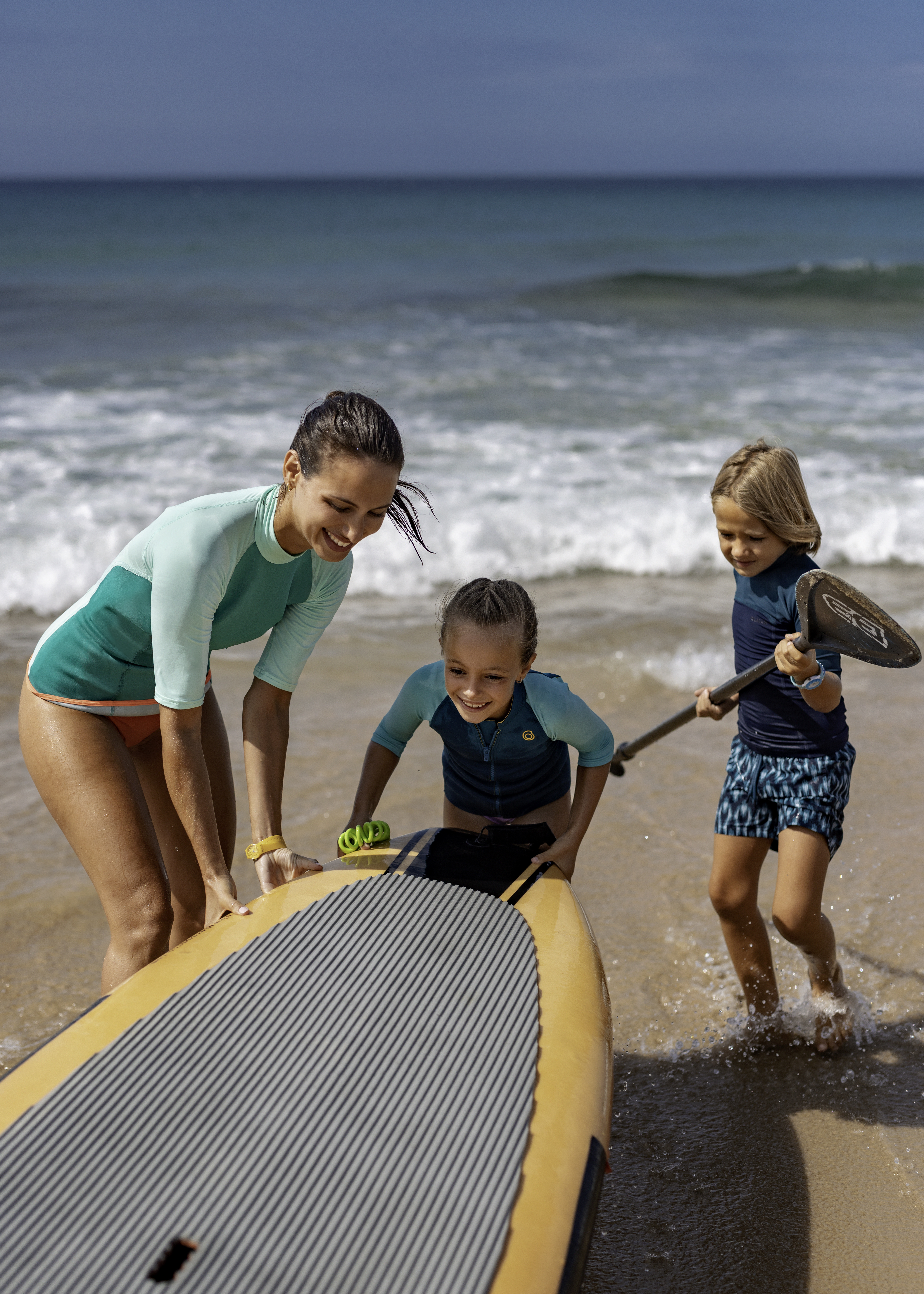 Smiling mother and kids launching stand-up paddleboard at the beach.