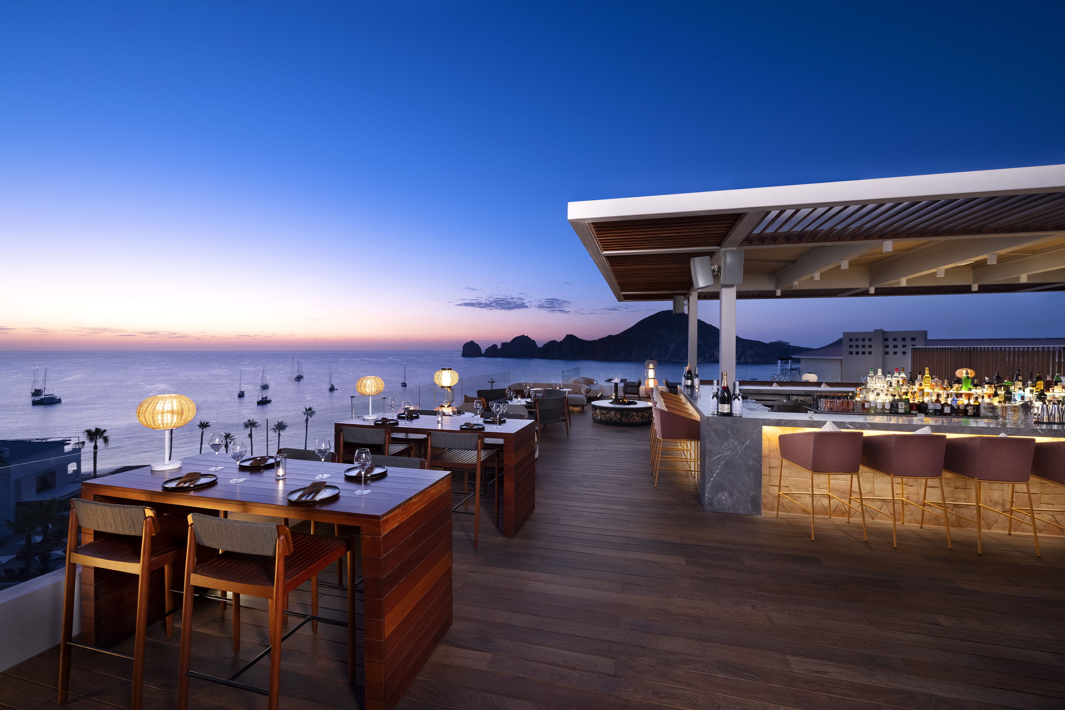 Cabo San Lucas rooftop bar with ocean, boats, and sunset view.