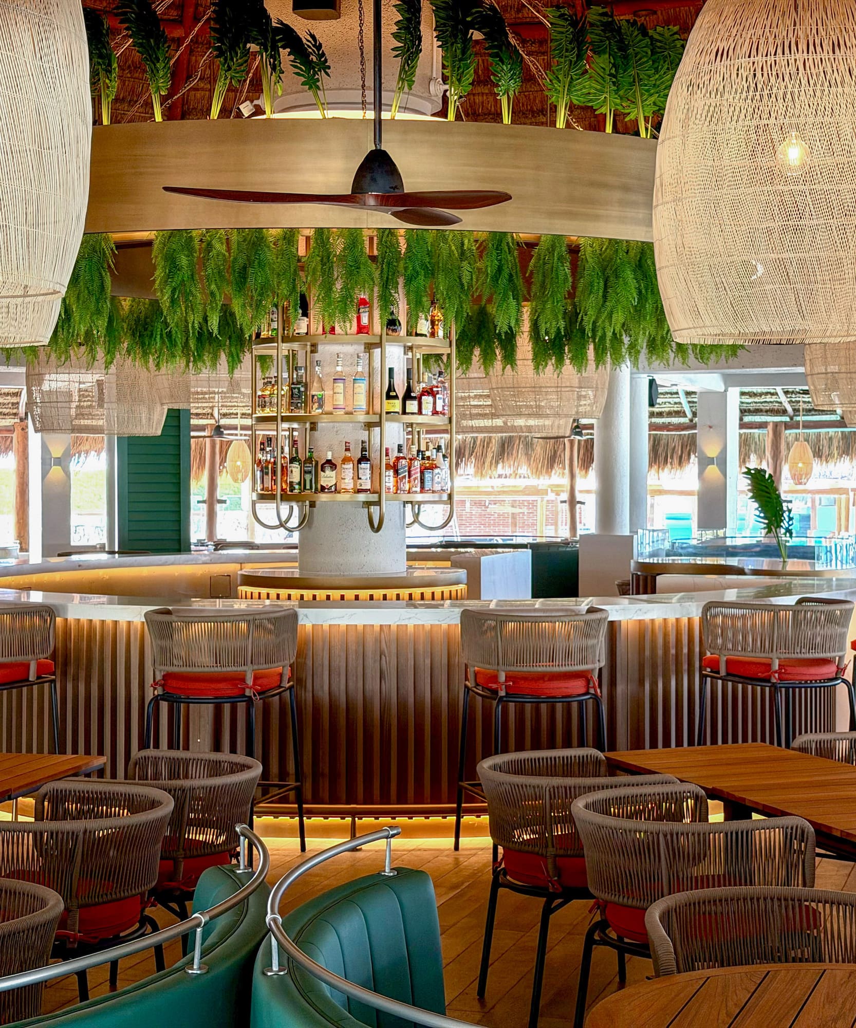 Stylish tropical bar with woven pendant lights, lush foliage, and modern seating.