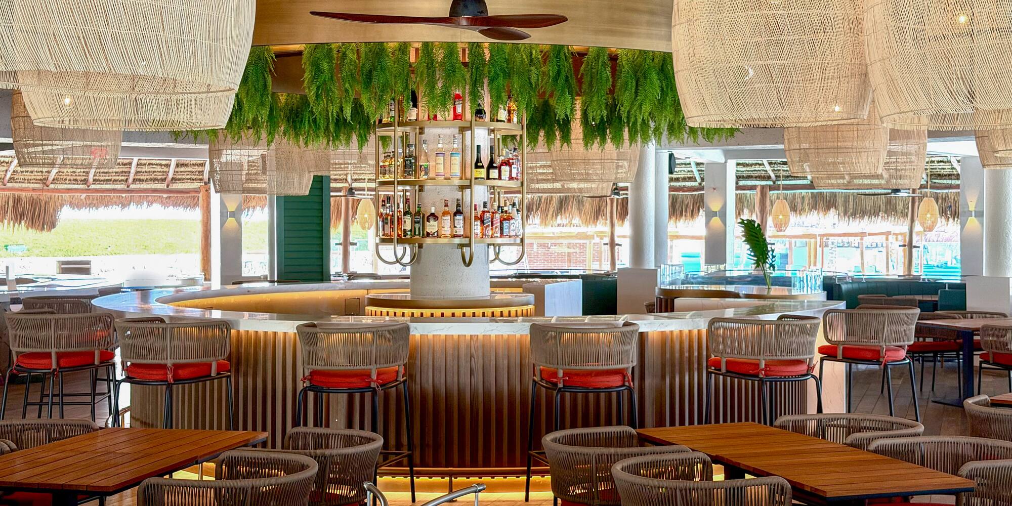 Stylish tropical bar with woven pendant lights, lush foliage, and modern seating.