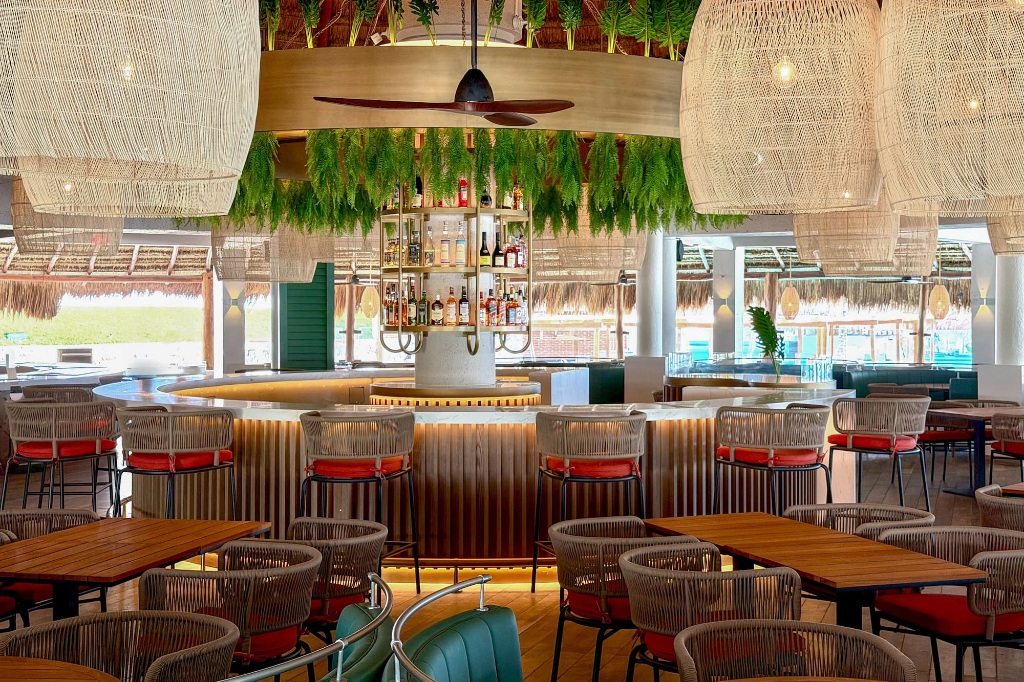 Tropical bar with rattan lights, lush plants, wood bar, and modern seating.