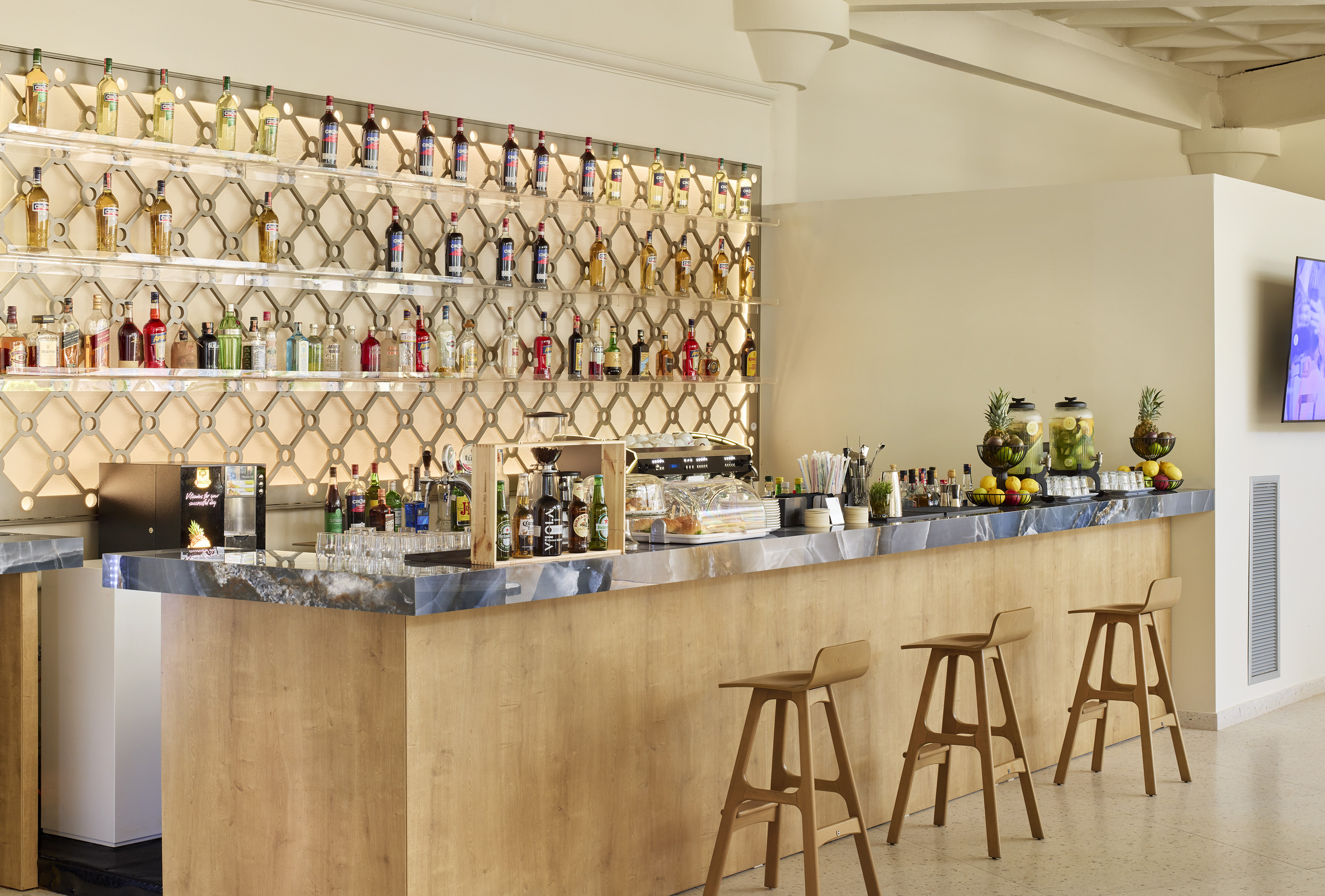 Modern bar with full liquor shelves, wooden counter, and fruit dispensers.