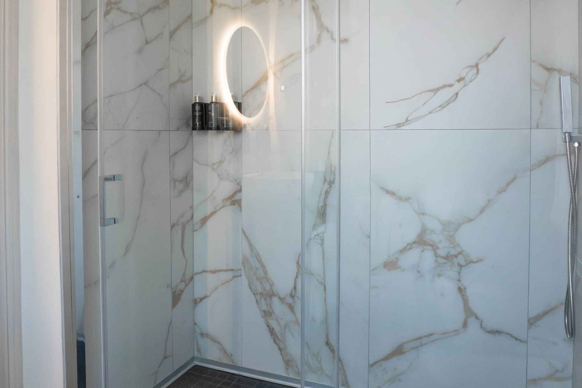 a glass shower with a round mirror